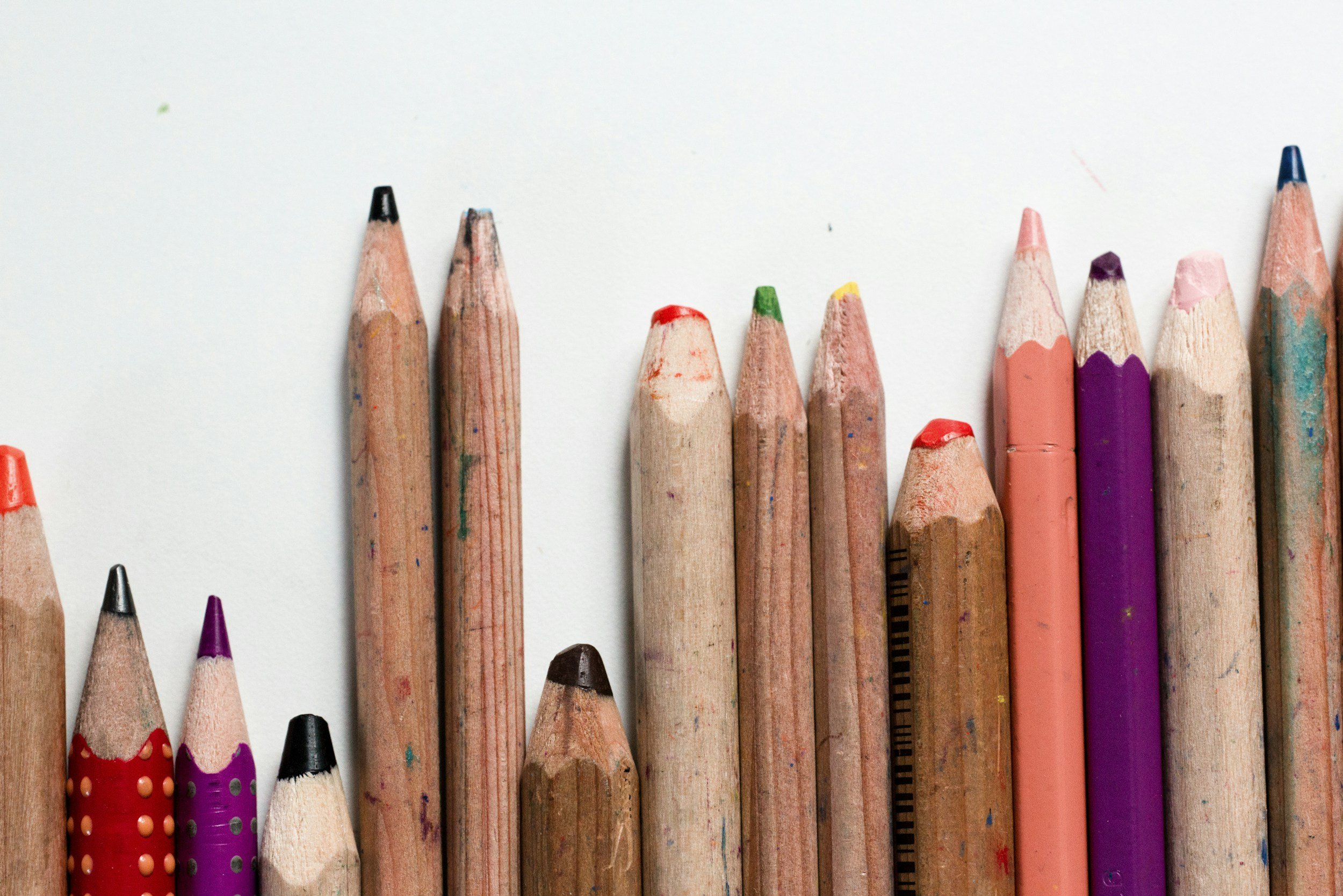 A row of colored pencils with sharpened tips, arranged on a white background.