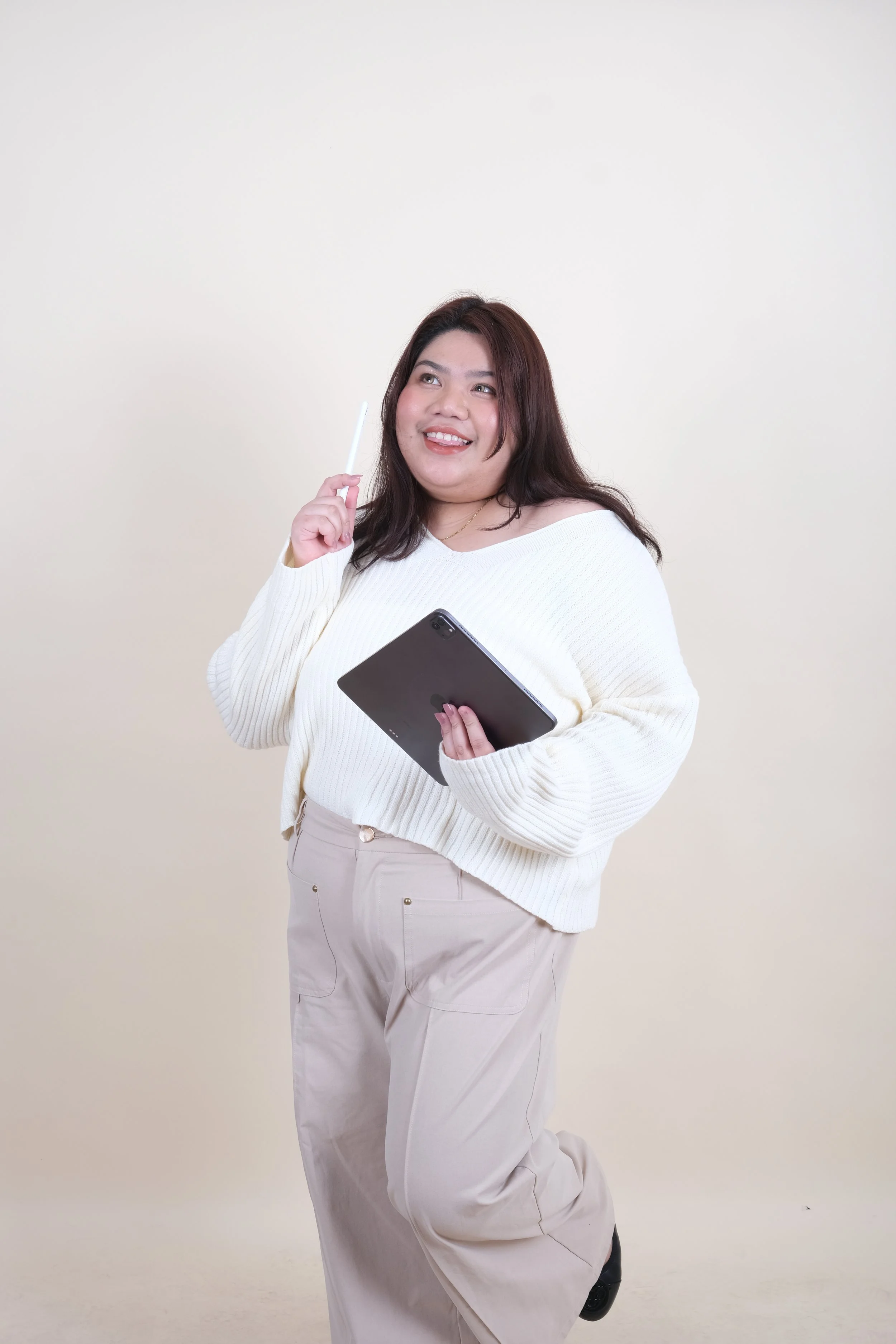 A woman holding a tablet and a pencil looking up with a smile.
