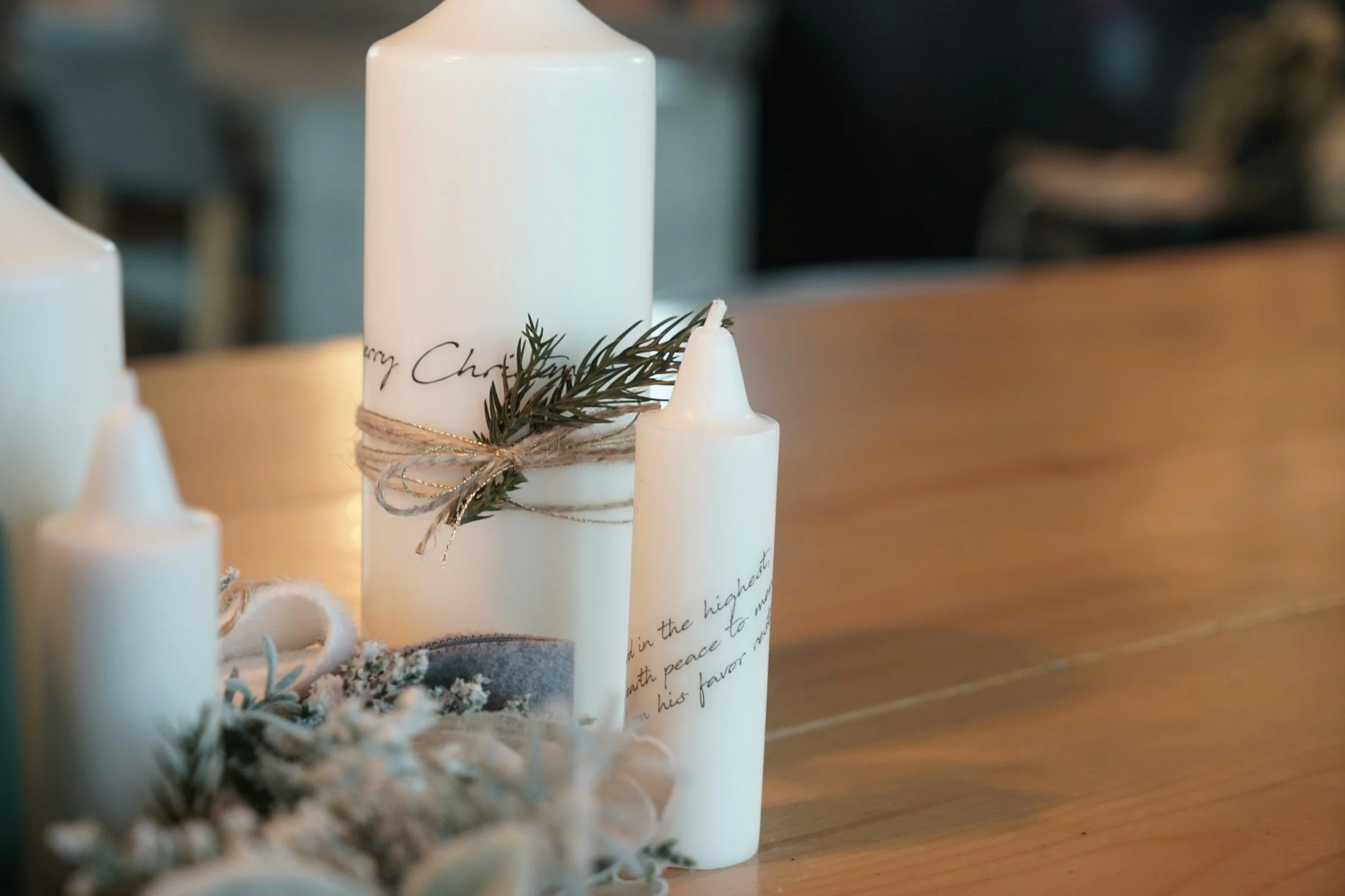 Weiße Kerzen, dekoriert mit Lacktwisten und Grün, stehen auf einem Holztablett. Die Kerzen sind für Weihnachten dekoriert.