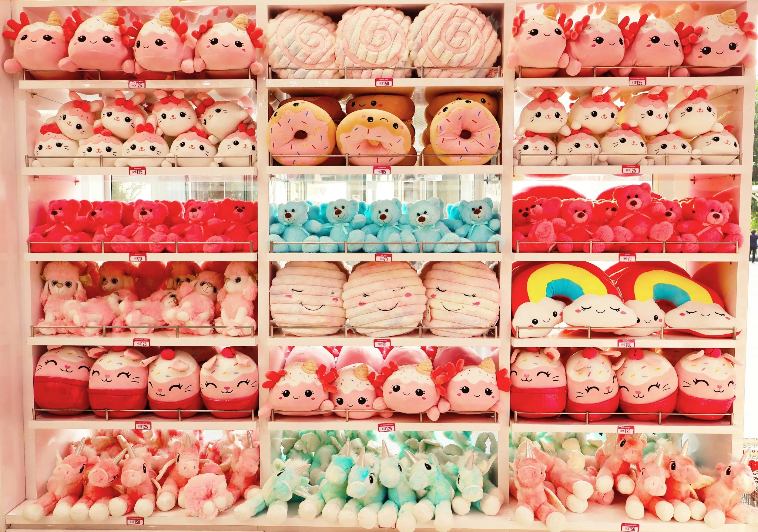 Regal mit bunten Plüschtieren, darunter Einhörner, Donuts, Pandabären, Teddys, lachende Eier, Regenbögen und Puscheltier-Variationen in verschiedenen Farben.