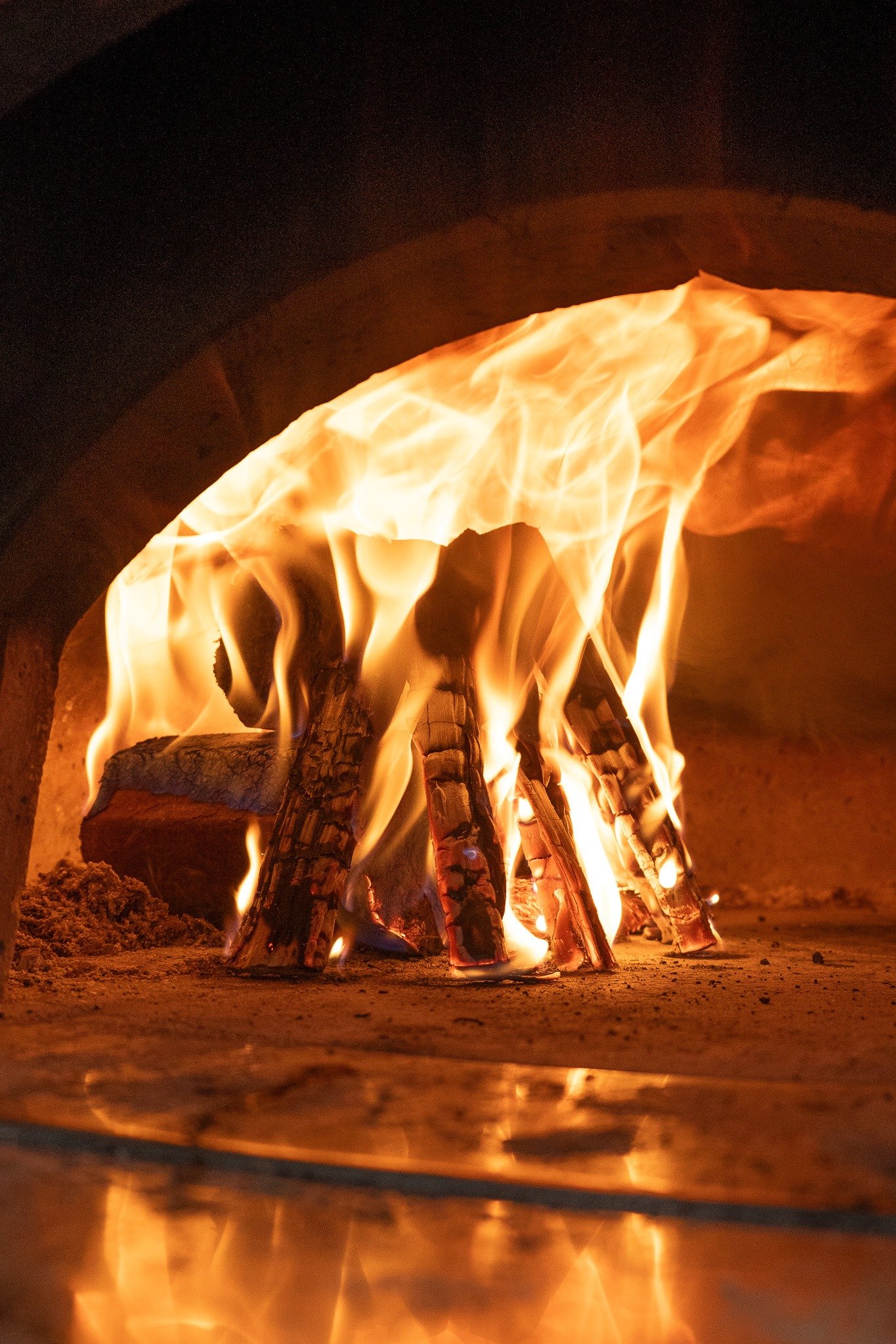 Close-up of a roaring campfire with wood logs burning inside a firepit, flames glowing vividly in a dark setting.