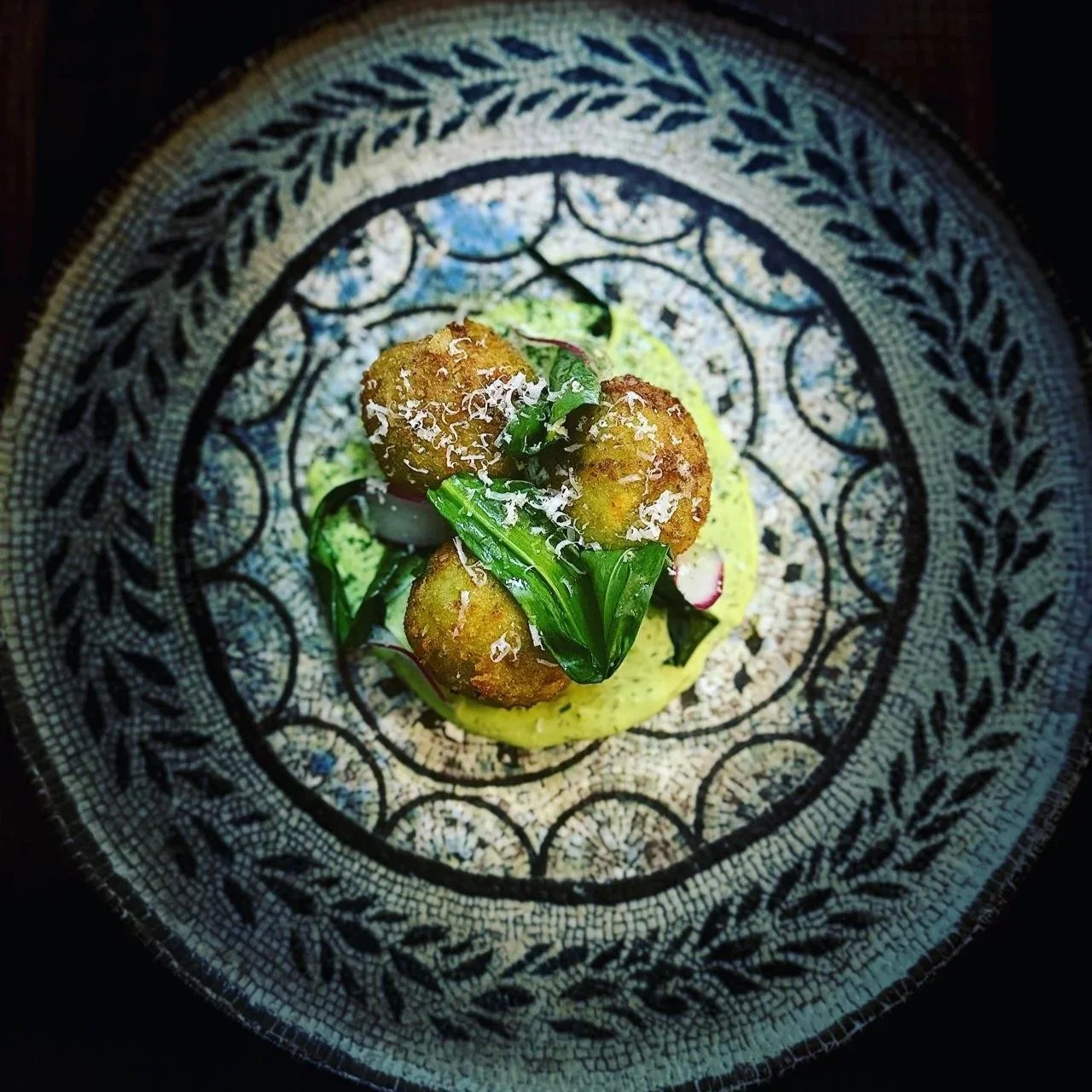 Fried food balls garnished with shredded cheese and green herbs on a bed of leafy greens, served on a decorative plate.