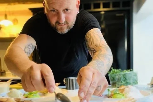 Man with tattoos preparing food in a kitchen.