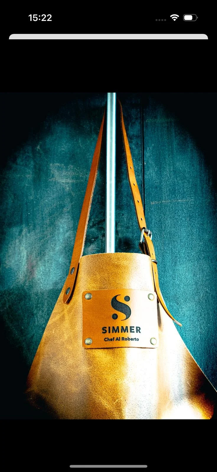 Leather tote bag with metal nameplate reading "SImmer Chef Al Roberto," hanging on a wall with a leather strap on a metal hook.