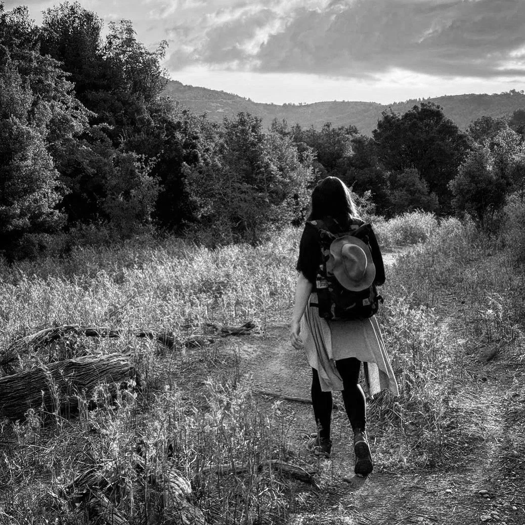 Frau mit Rucksack wandert auf einem Waldweg in der Natur bei Sonnenuntergang.