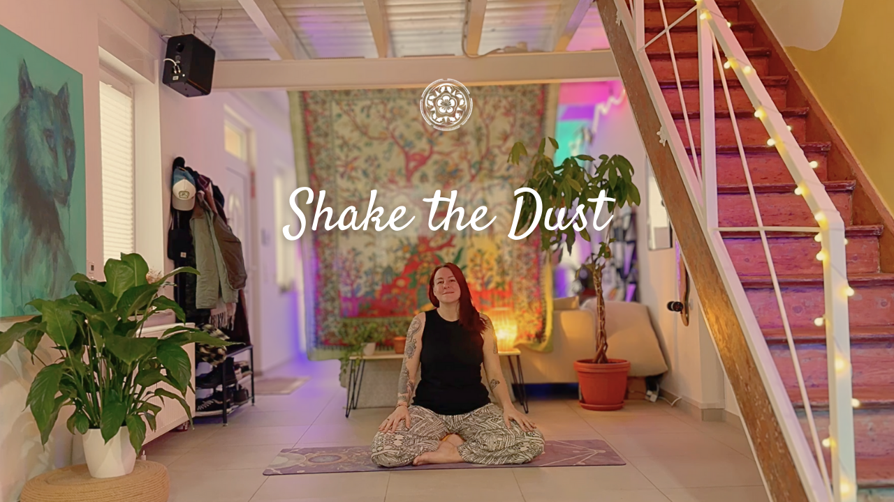 Eine Frau sitzt im Lotussitz auf einem Yogamatte in einem gestimmten Raum mit Pflanzen, Wandbehang und Treppe, die mit Lichterketten dekoriert ist, mit dem Text "Shake the Dust" darüber.