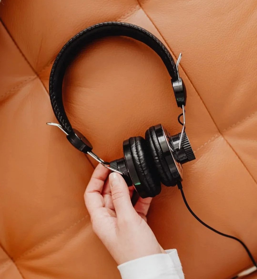 Ein Paar schwarze Over-Ear-Kopfhörer, die auf einem braunen Lederpolster liegen, wobei eine Hand sie hält.