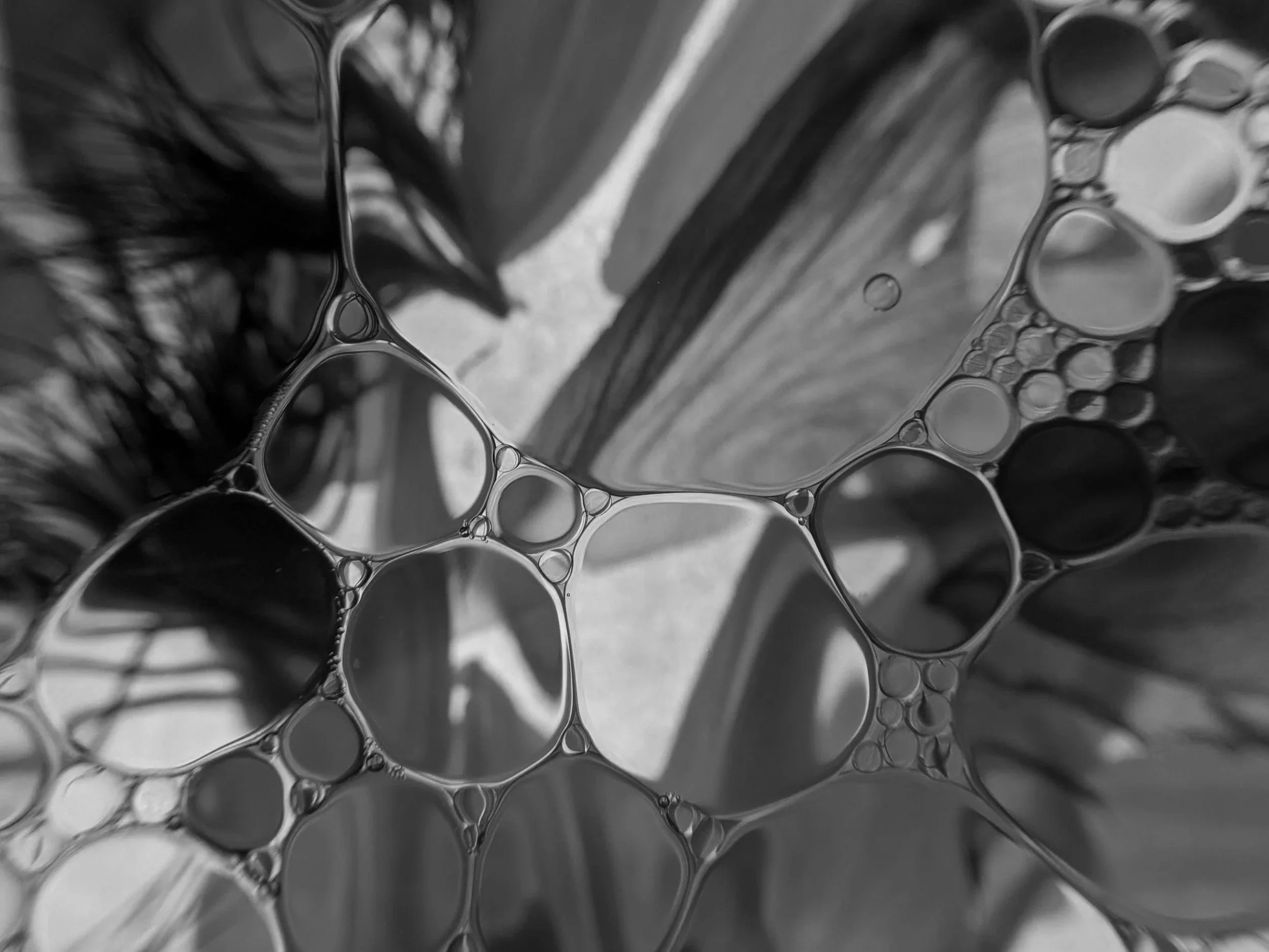 Nahaufnahme von Seifenblasen auf einer Oberfläche, mit verschiedenen Größen und einer spiegelnden Oberfläche, in Schwarzweiß gehalten.