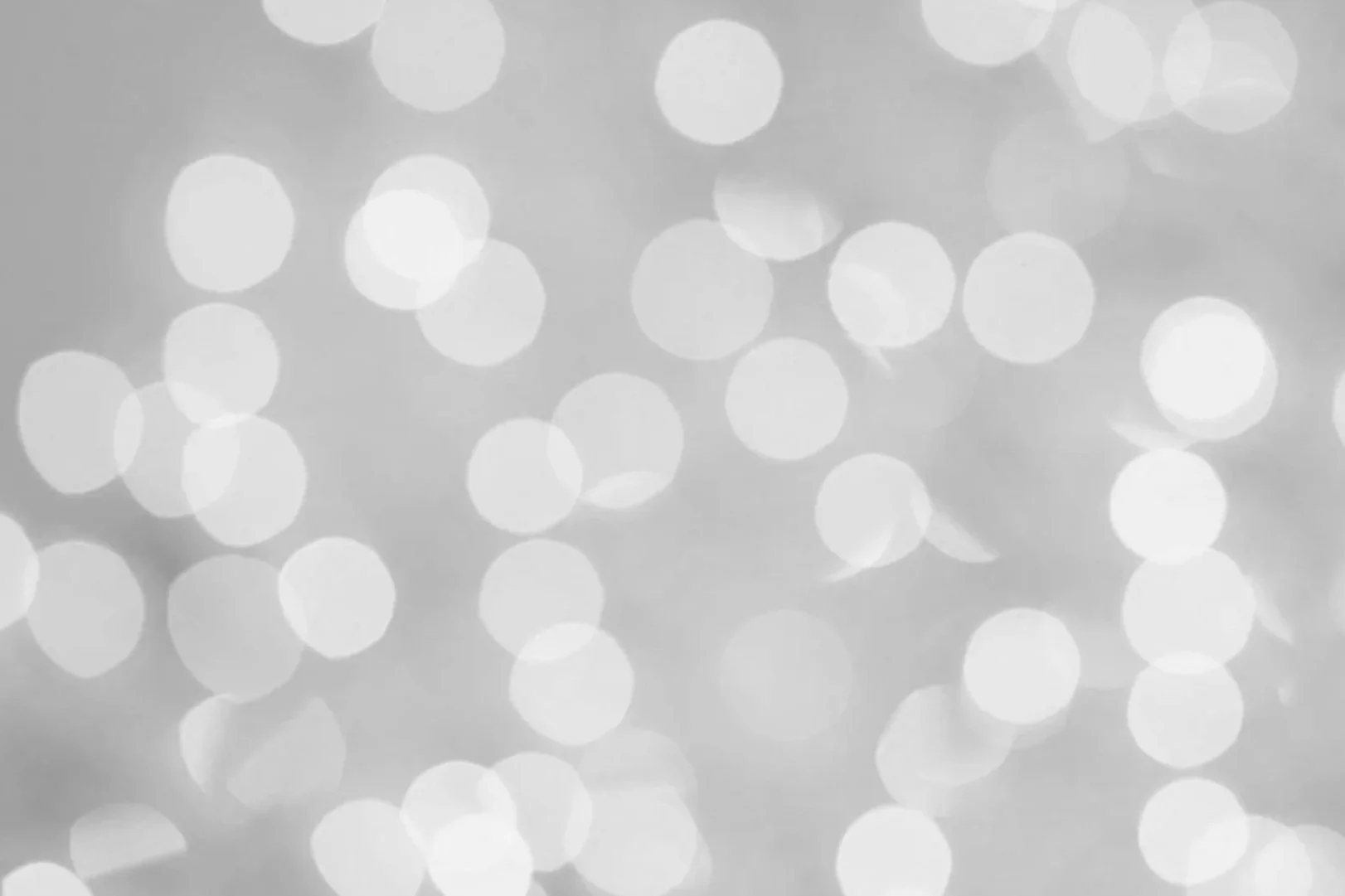 Unschärftes Bild mit weißen Lichtpunkten auf grauem Hintergrund, Bokeh-Effekt.