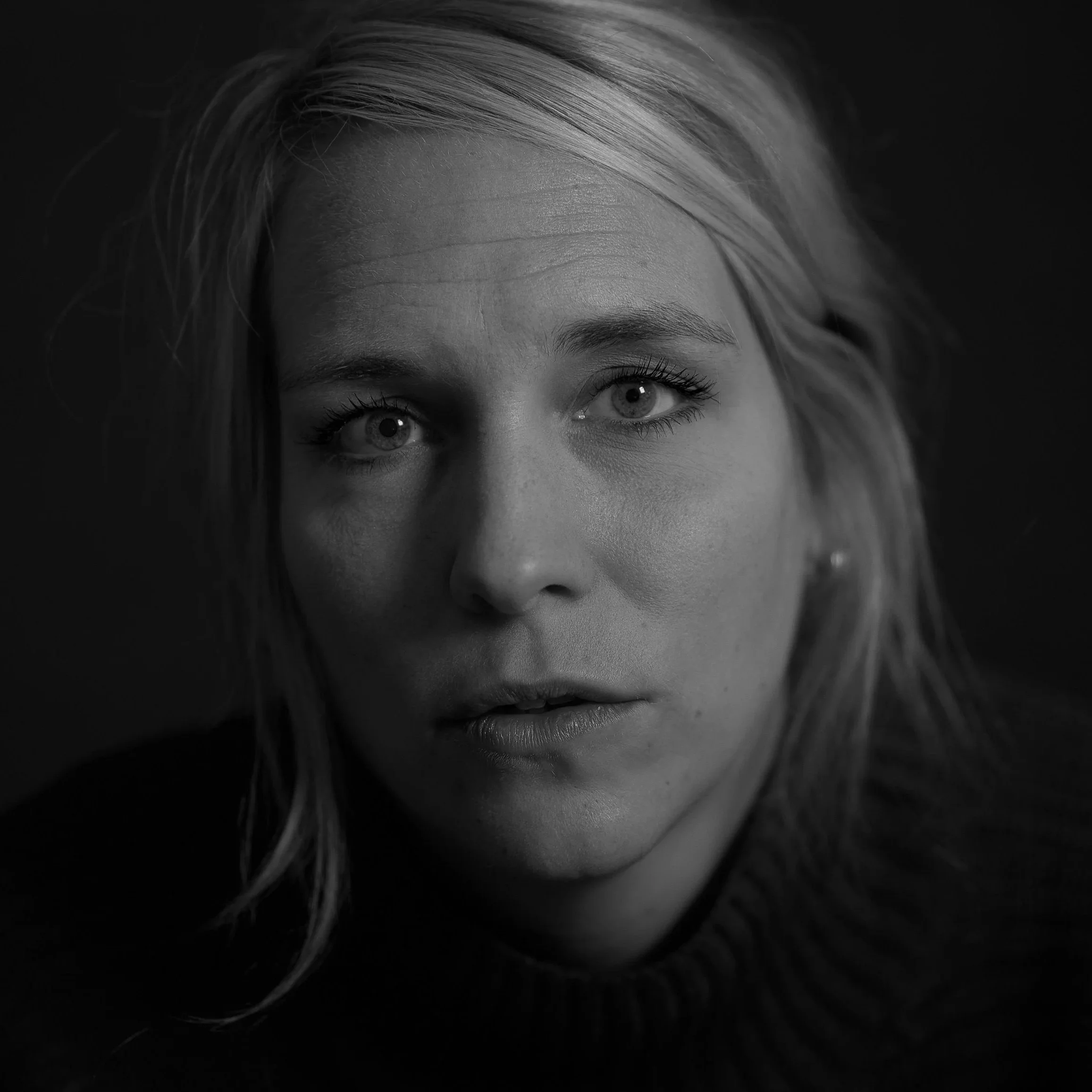 Schwarz-weiß-Porträt eines jungen Mädchens mit blonden Haaren und blauen Augen, das direkt in die Kamera schaut.