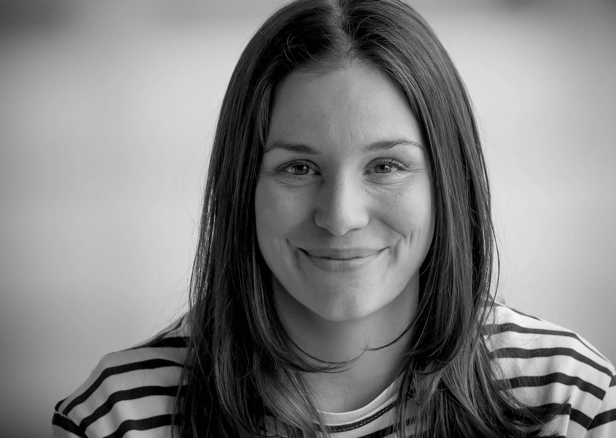 Schwarze und weiße Fotografie eines lächelnden Frauengesichts, tragend ein gestreiftes Hemd mit Knopfkragen.