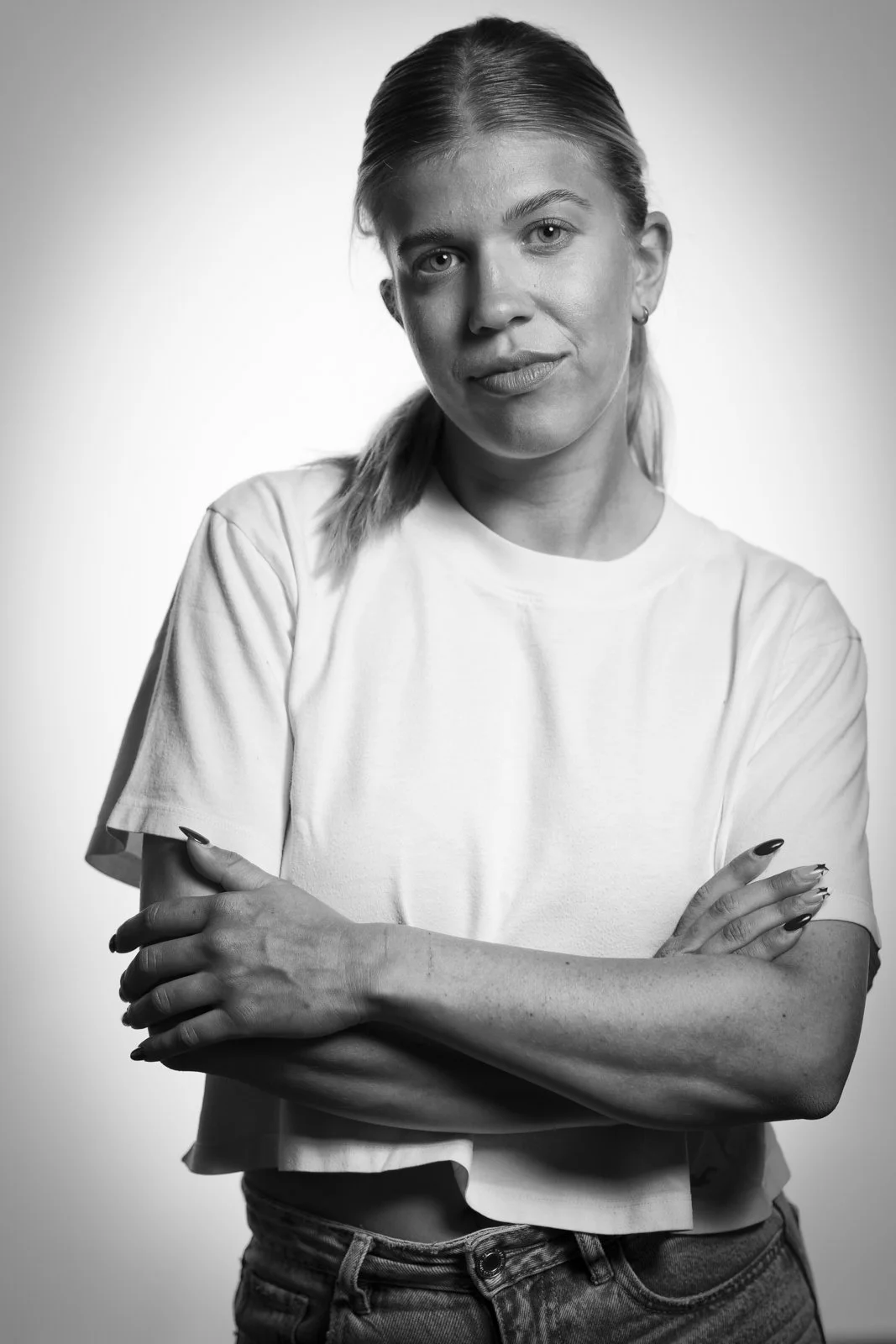 Schwarz-Weiß-Foto einer Frau, die in die Kamera schaut, Arme verschränkt und einen weißen T-Shirt trägt.