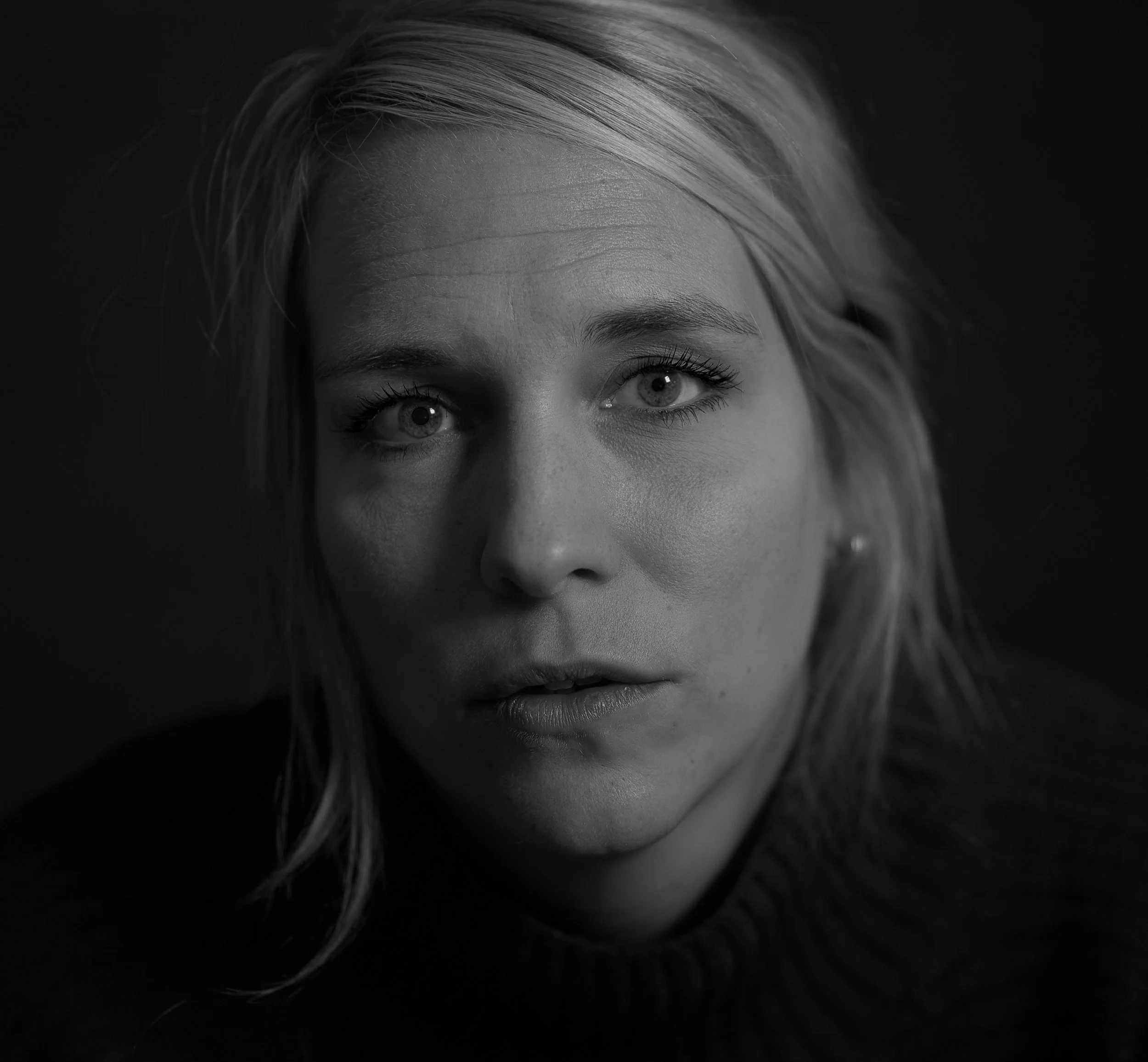 Schwarz-weiße Nahaufnahme eines Gesichts einer Frau mit blondem Haar und blauen Augen, getragen in einem dunklen Pullover.