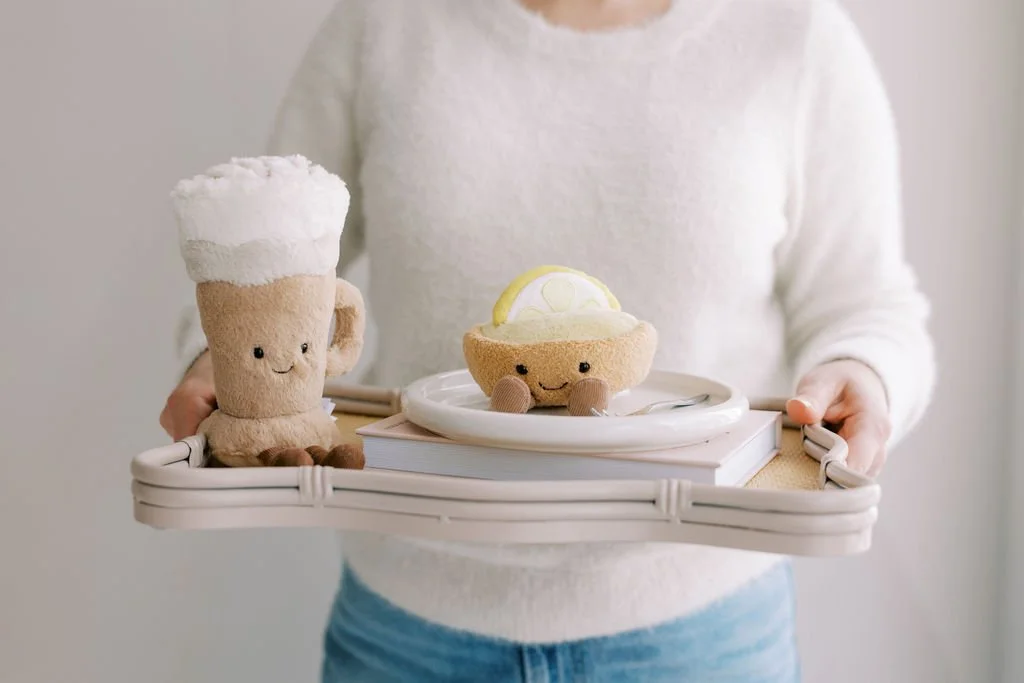 Person holding a tray with plush toy drinks and cupcakes that have smiling faces