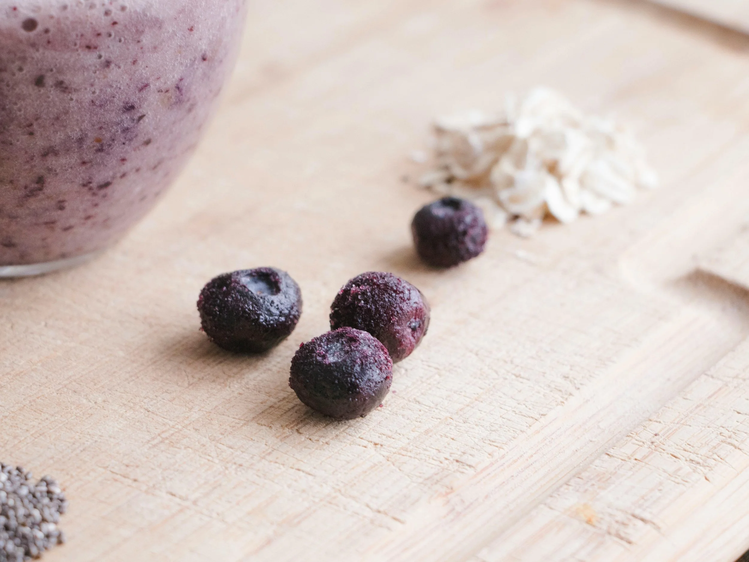 Frozen blackberries, oatmeal, and chia seeds on a wooden cutting board with a purple smoothie in the background.