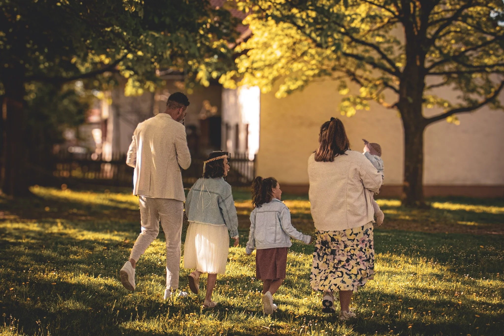 Familie mit zwei Erwachsenen und zwei Kindern geht im Park im Sonnenuntergang spazieren, unter Bäumen mit goldgelbem Wetter