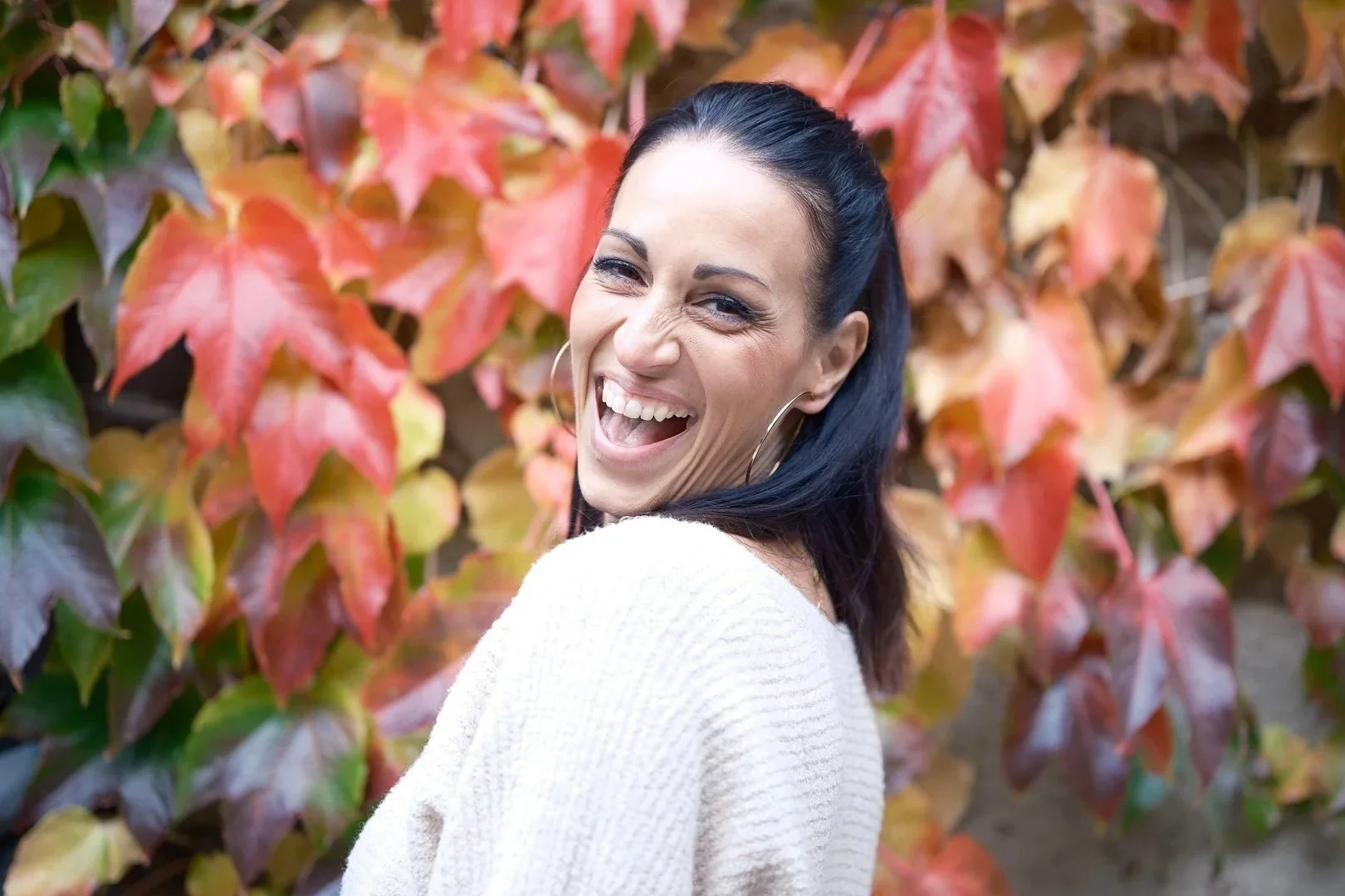 Junge Frau lacht lachend vor buntem Herbstlaub.