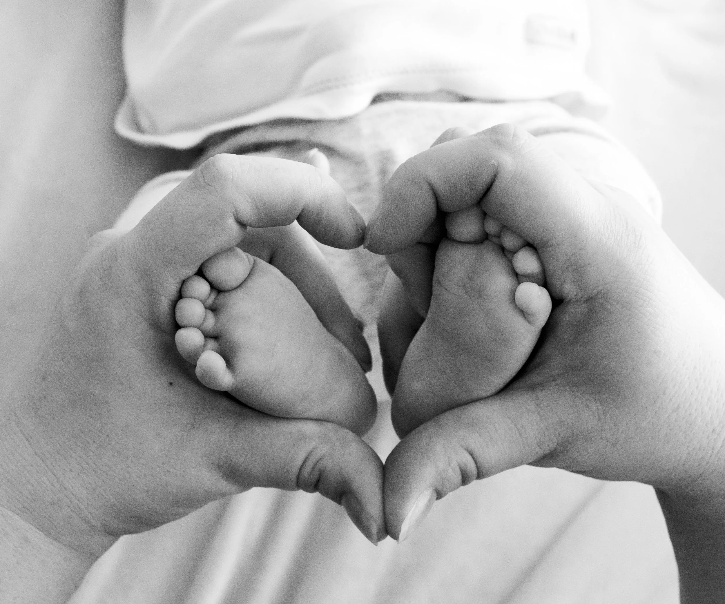 Zwei Hände formen ein Herz, in dessen Mitte Babys Füße sichtbar sind.