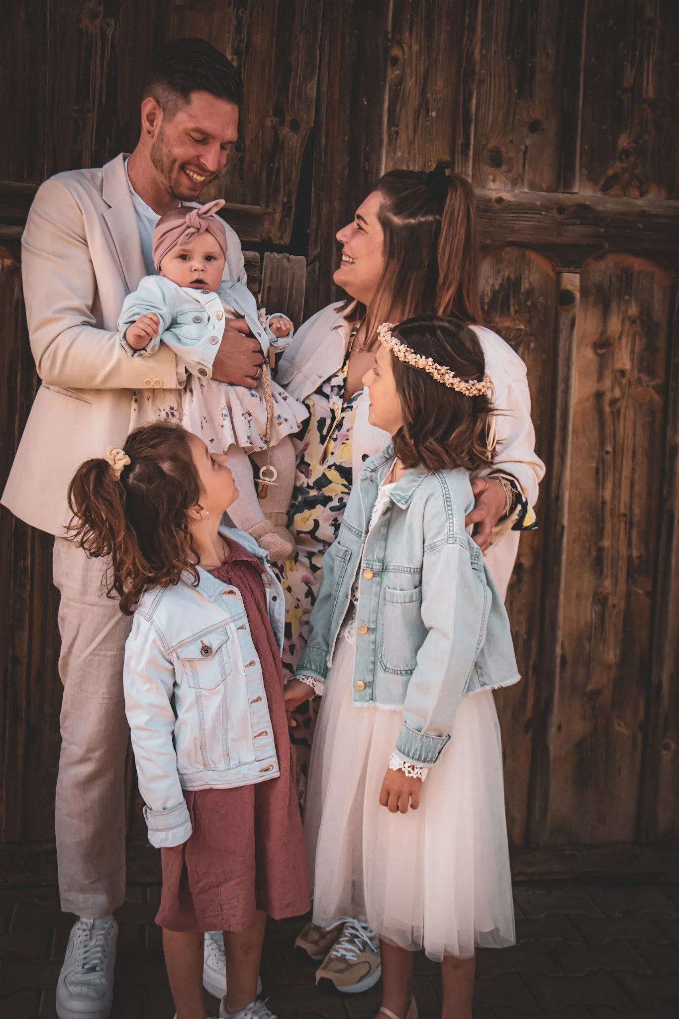 Familie steht vor einer Holzlatzwand, alle lachen und schauen sich an.
