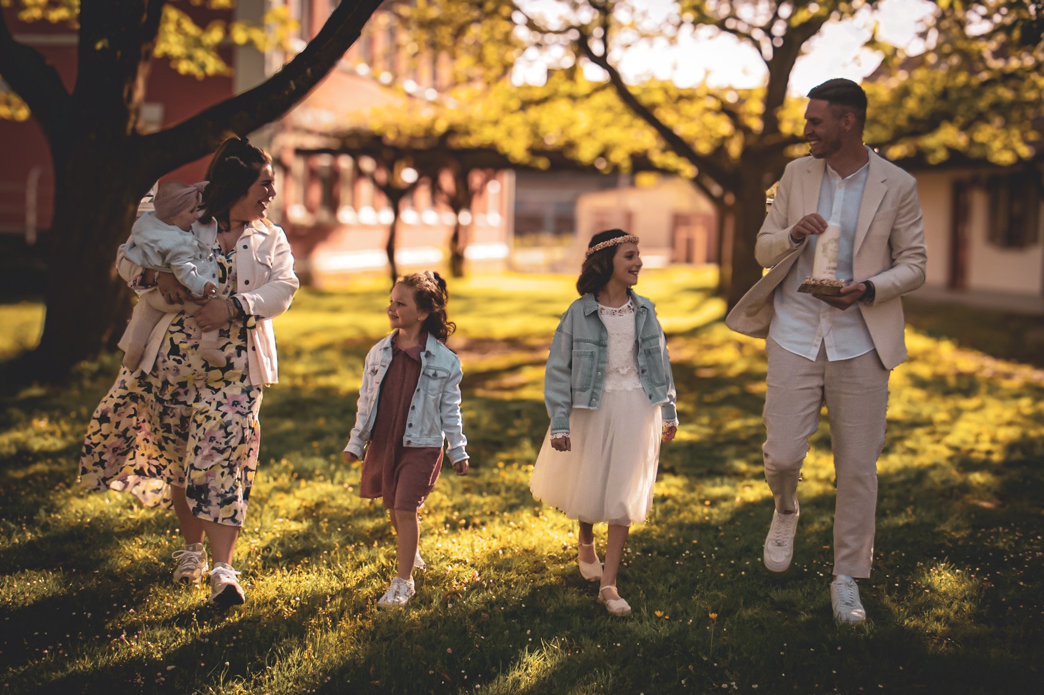 Familie beim Spaziergang im Park bei Sonnenuntergang, inklusive Mutter, Vater, zwei Töchter und Kleinkind.
