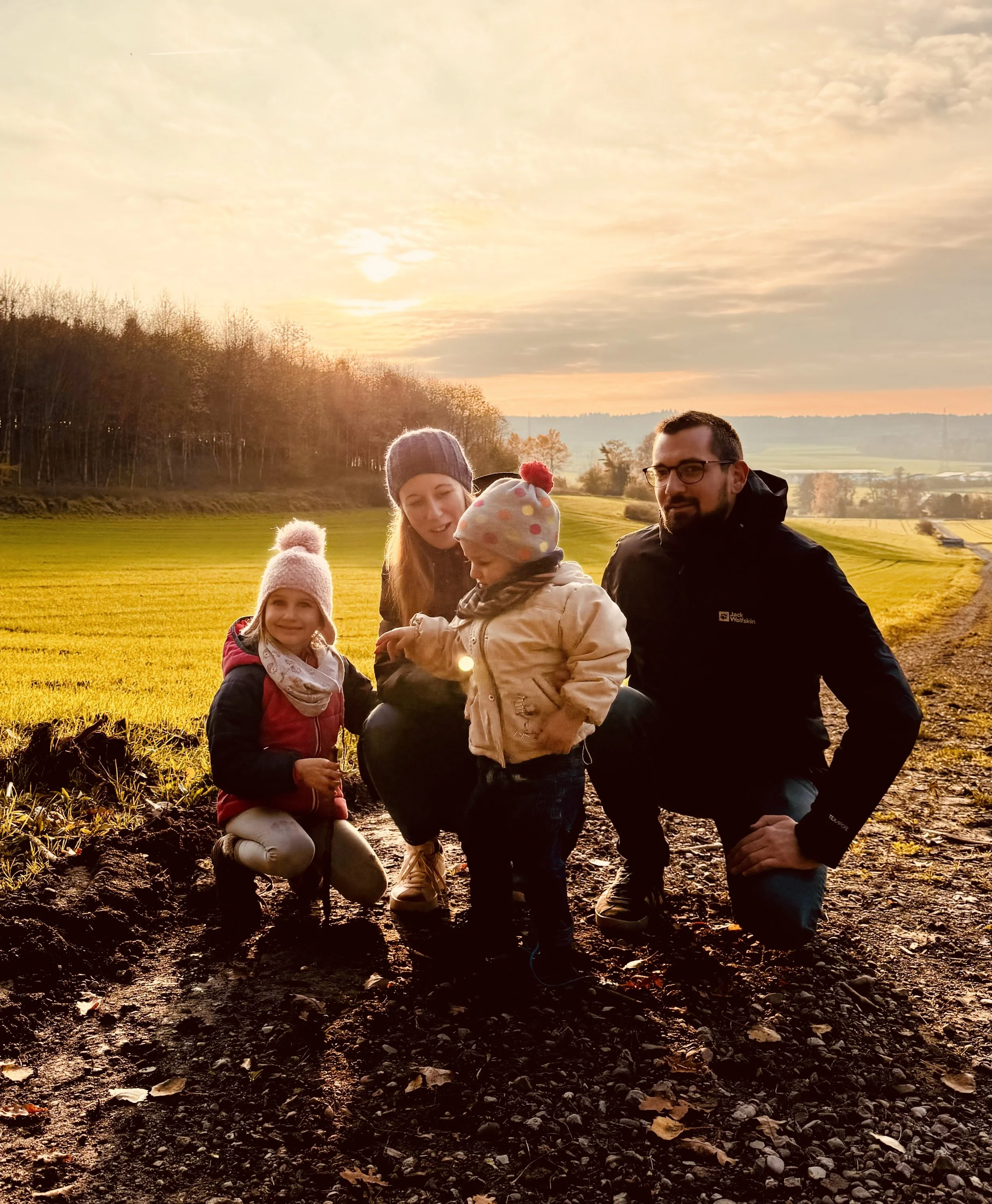 Familie mit zwei Kindern bei Sonnenuntergang in einer offenen Landschaft