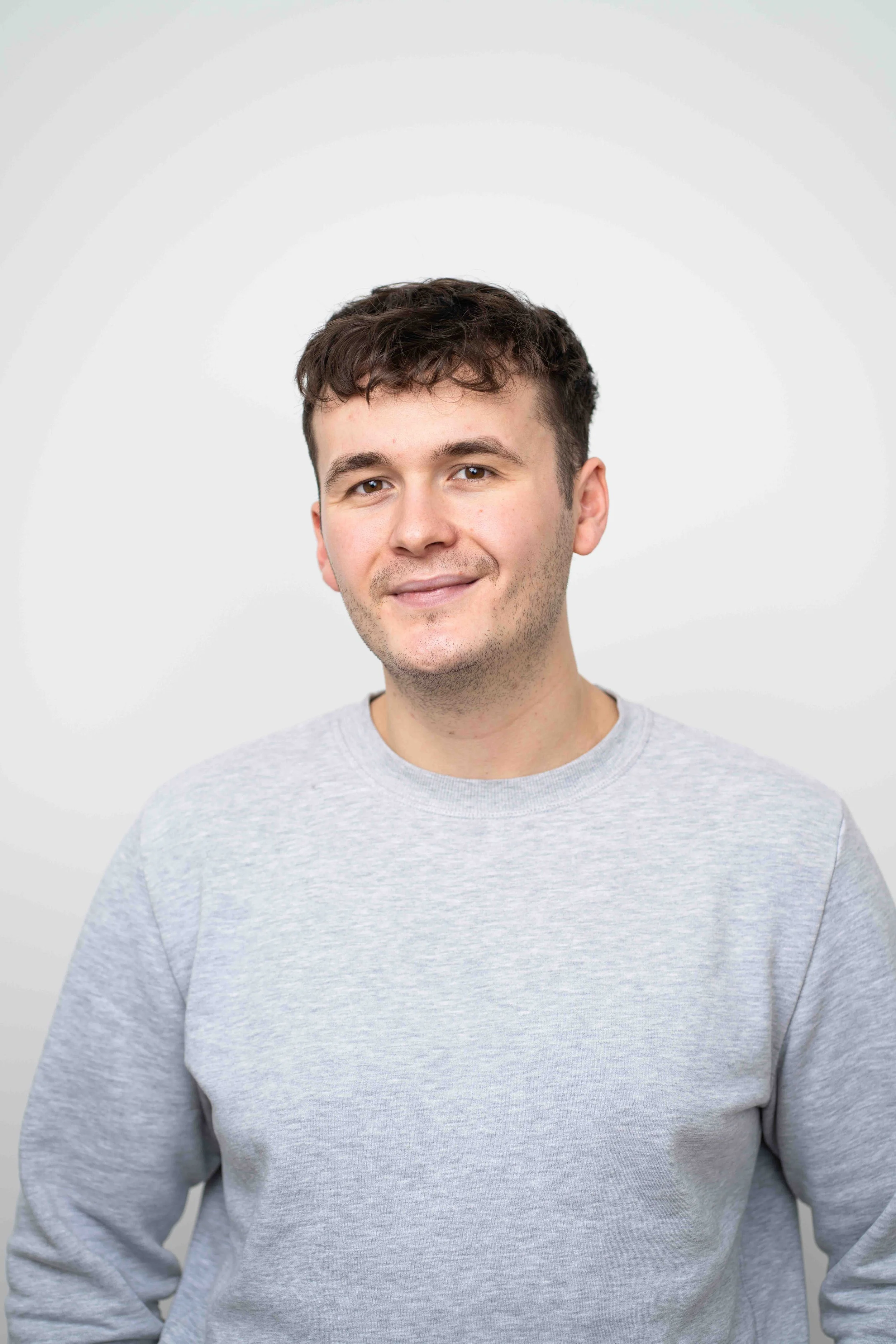 Der Psychotherapeut trägt ein graues Sweatshirt, lächelt leicht und blickt freundlich in die Kamera vor einem neutralen weißen Hintergrund.