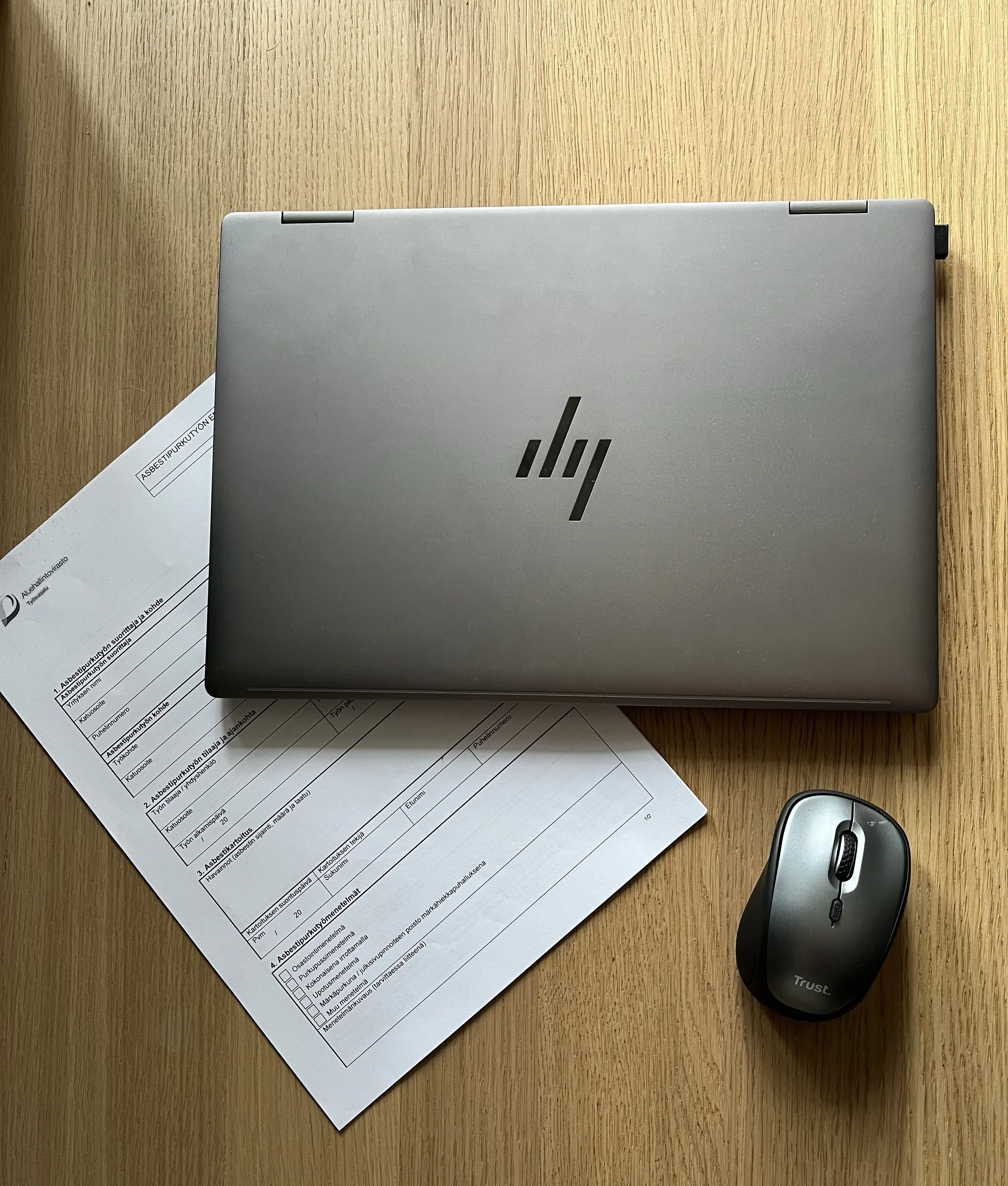 Kannettava tietokone, hiiri ja paperilomake pöydällä.