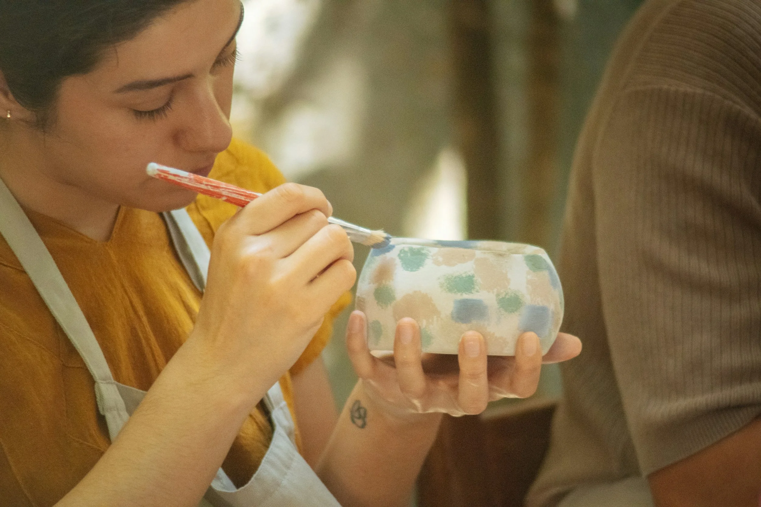 A woman painting an unglazed piece of pottery