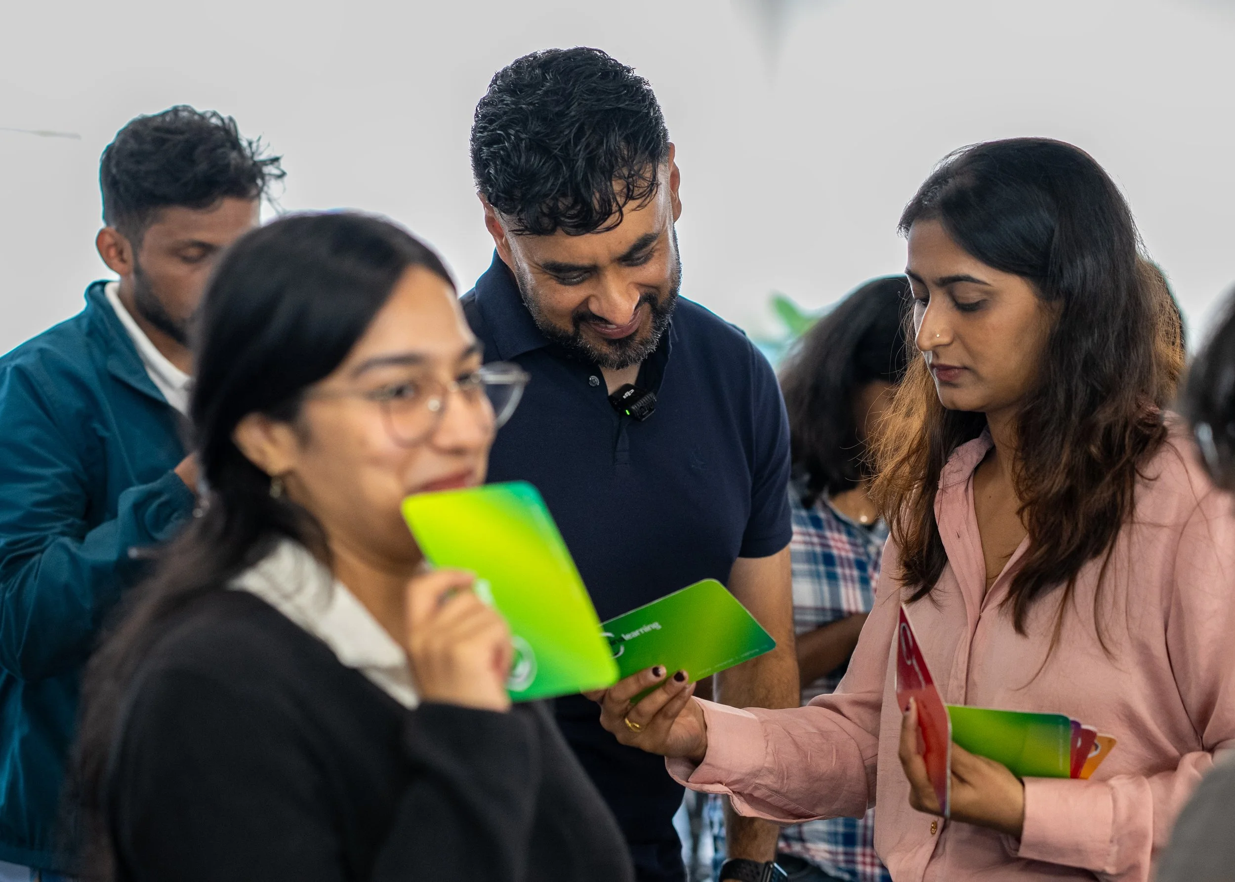 A group of diverse people gathered, holding green pamphlets and engaging in conversation, at an indoor event.