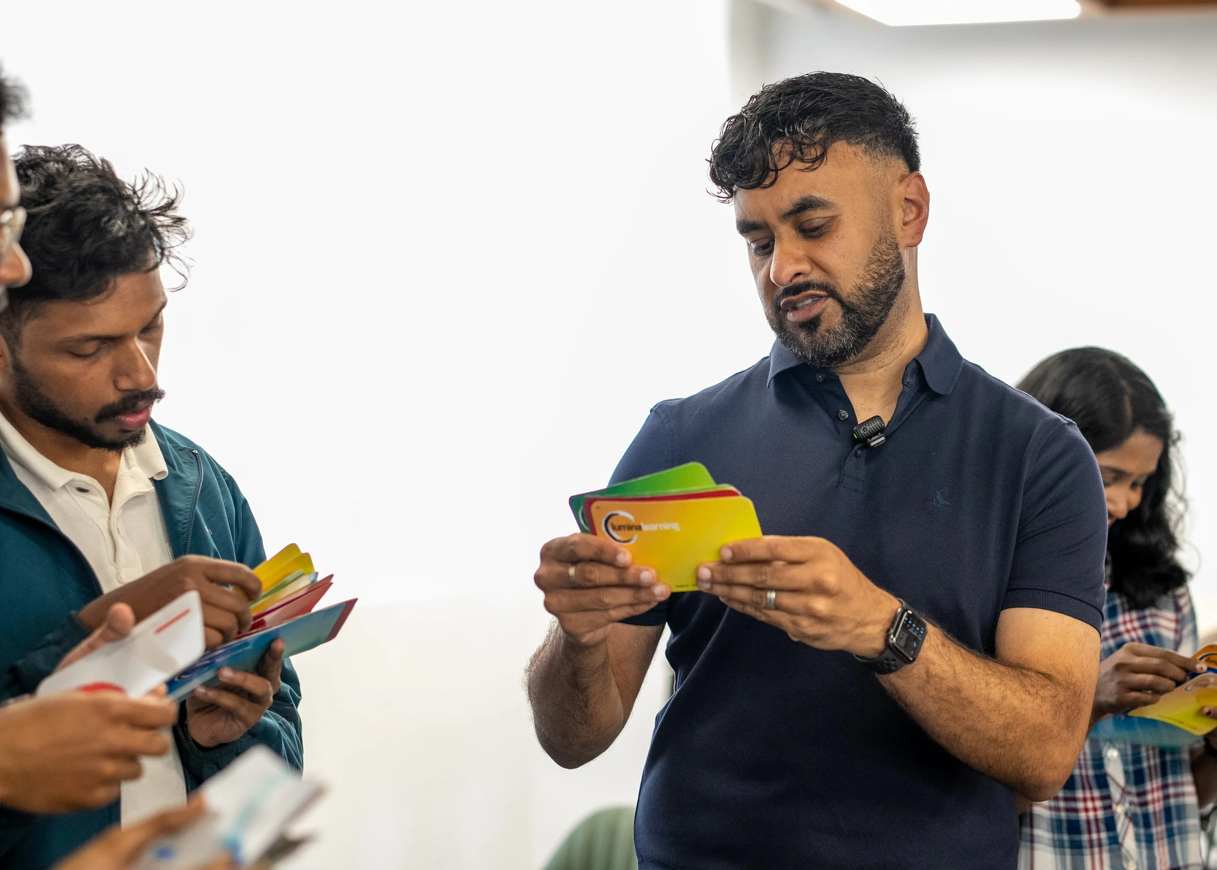 Group of people, primarily men, holding and looking at colorful cards or options, in a professional or educational setting, with a focus on the man in a navy blue shirt.