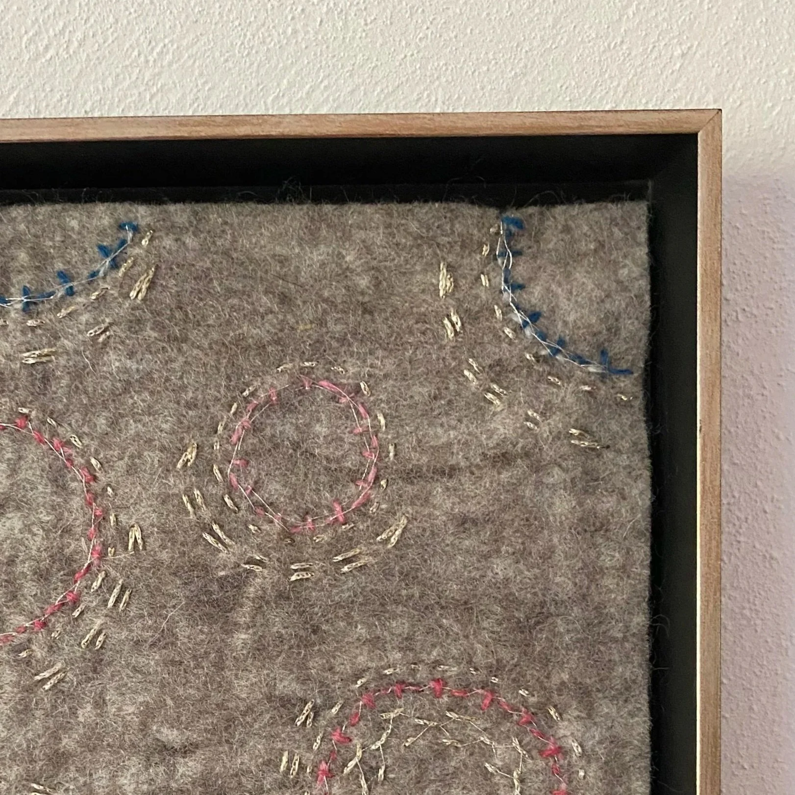 Ein T display mit buntem Stickmuster auf Filzstoff. Der Rahmen besteht aus Holz.
