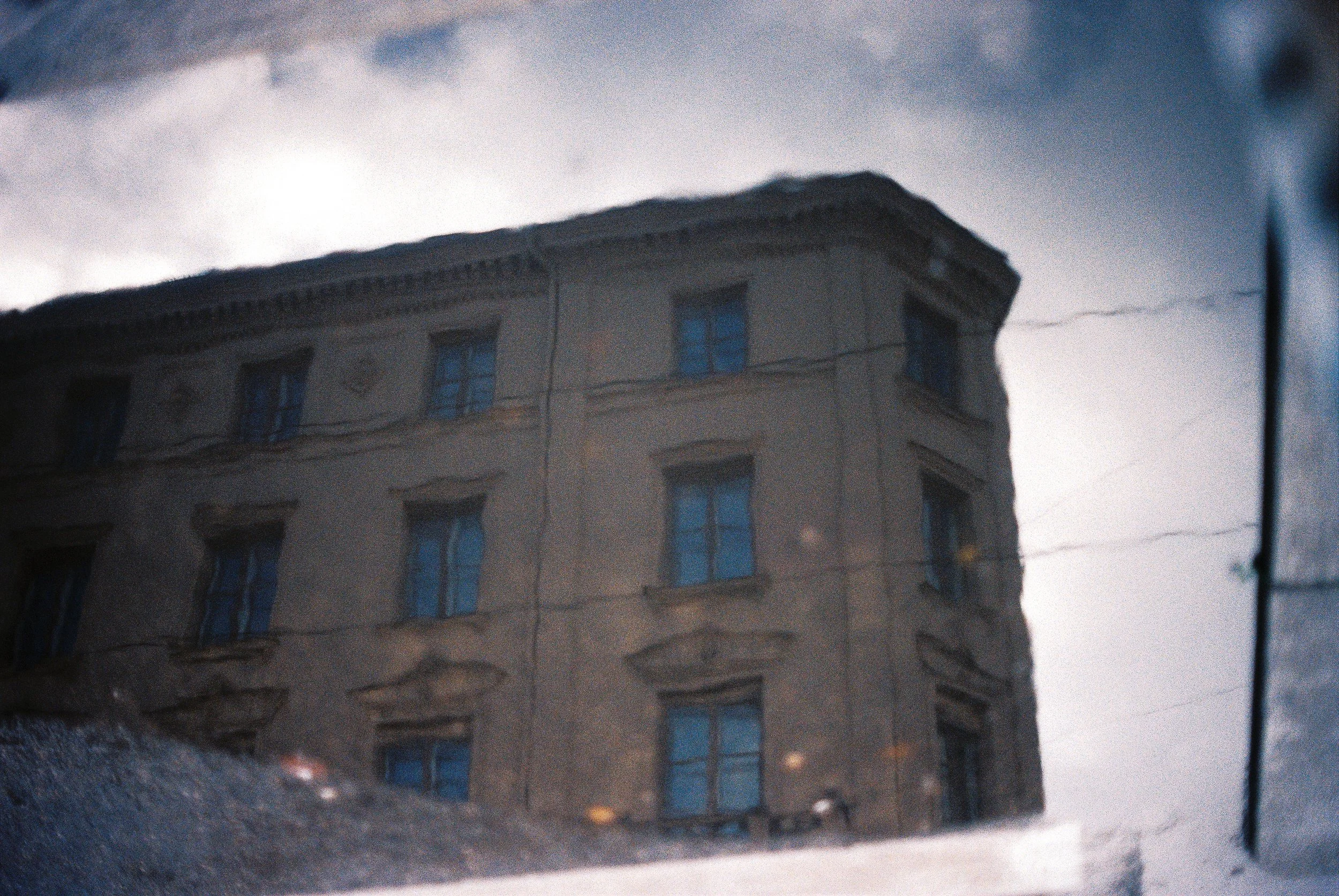 Ein Gebäude mit mehreren Fenstern, das durch eine rissige Glasscheibe betrachtet wird, mit Himmel und Wolken im Hintergrund.