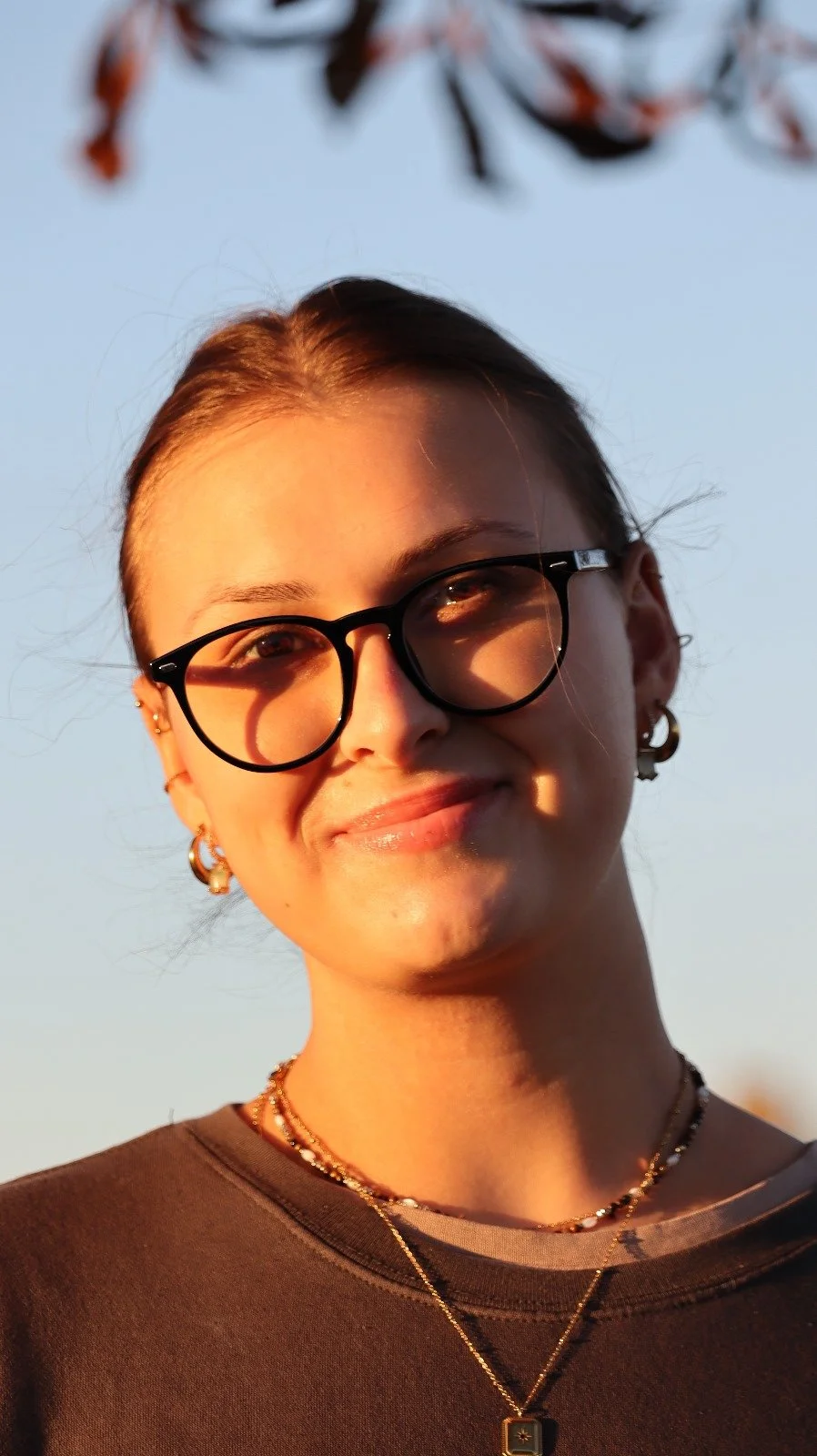 Junge Frau mit Brille und Schmuck, Sonnenuntergang, blauer Himmel.