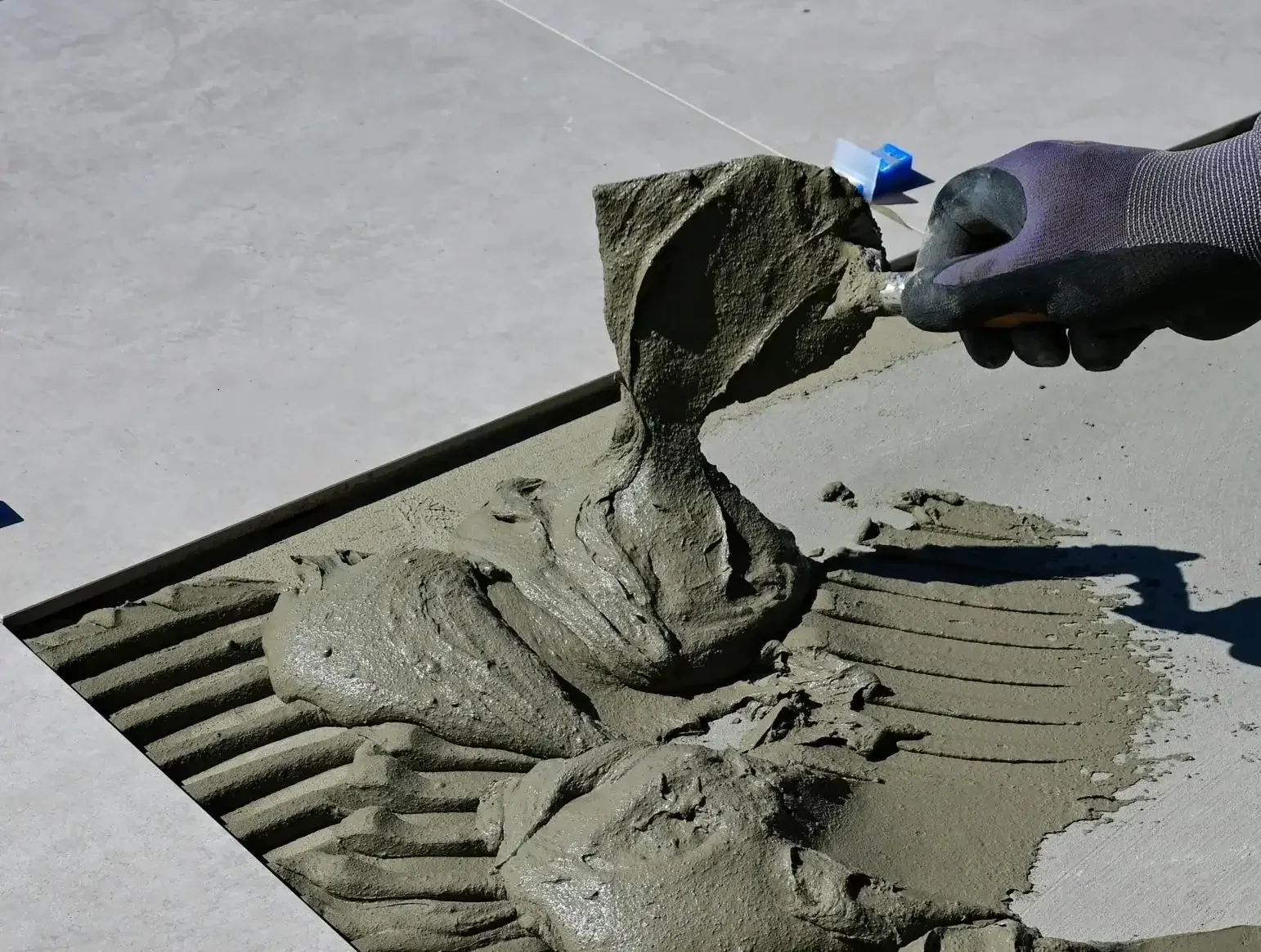 A person wearing black gloves is smoothing wet cement with a trowel, creating a fossil-like impression of a skeleton on the concrete surface.