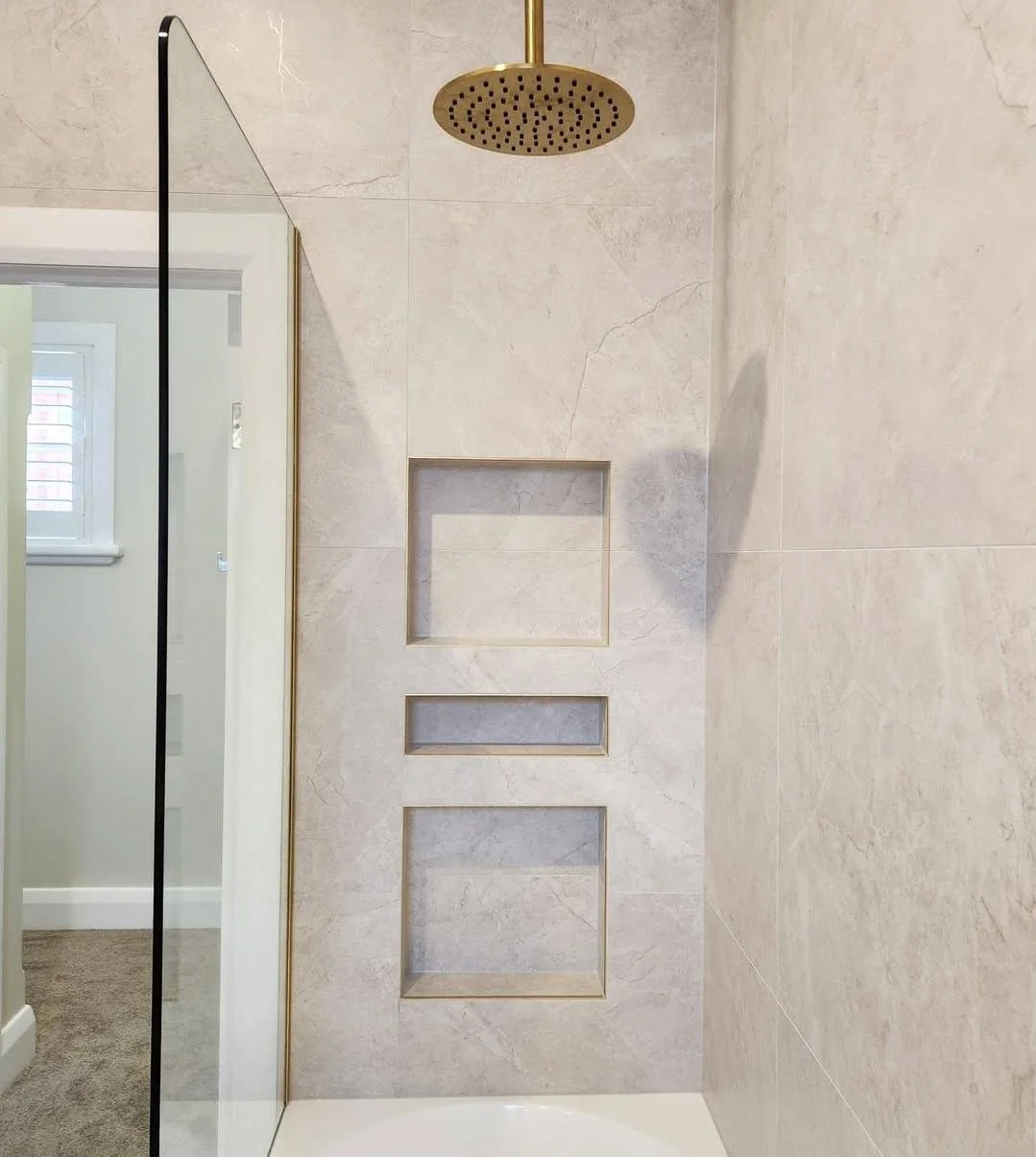 Close-up of a shower wall with a built-in niche, a round rainfall showerhead, and minimalistic design.