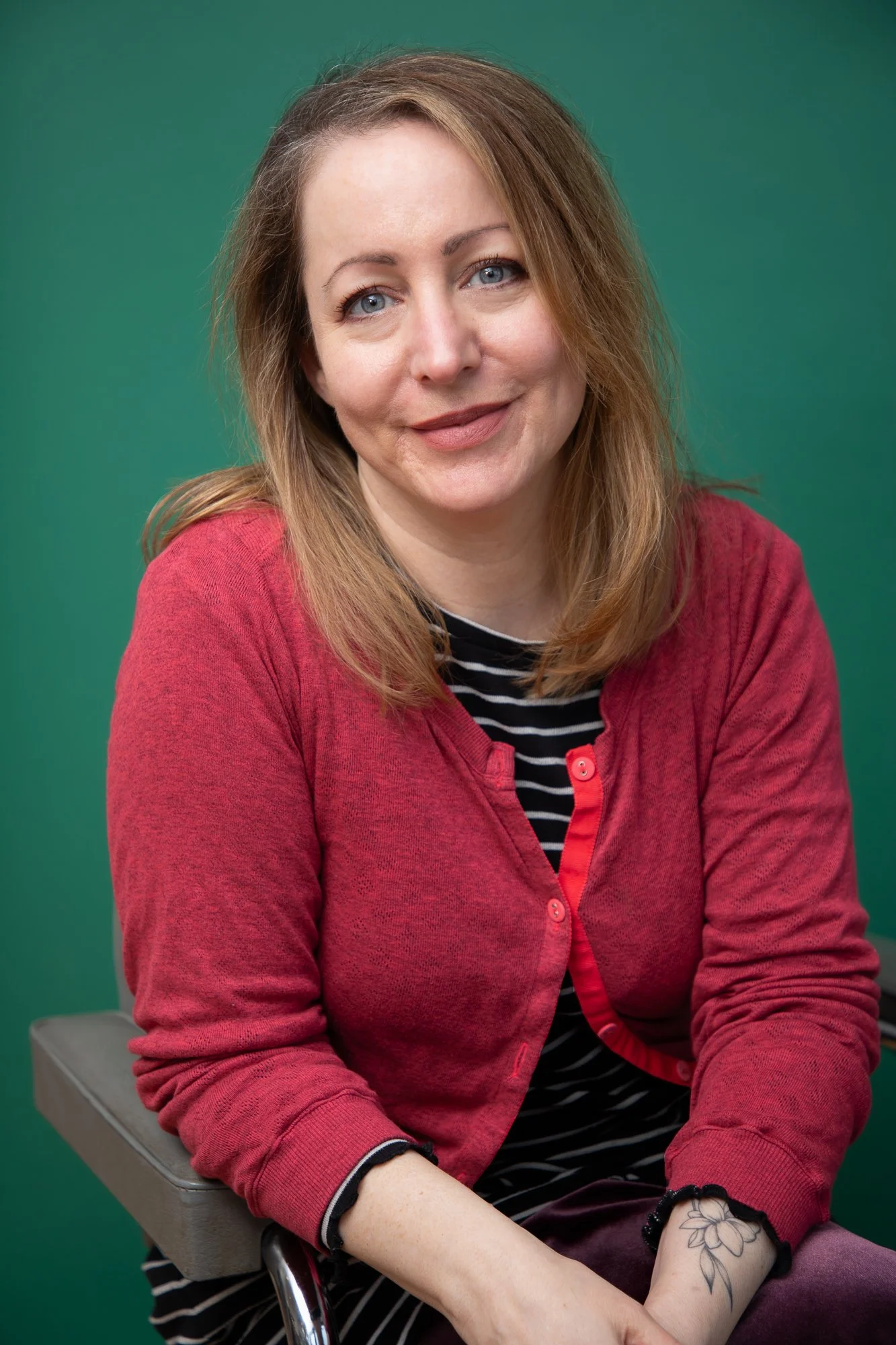 Yasmeen is smiling warmly, she is wearing a stripy top with a bright pink cardigan