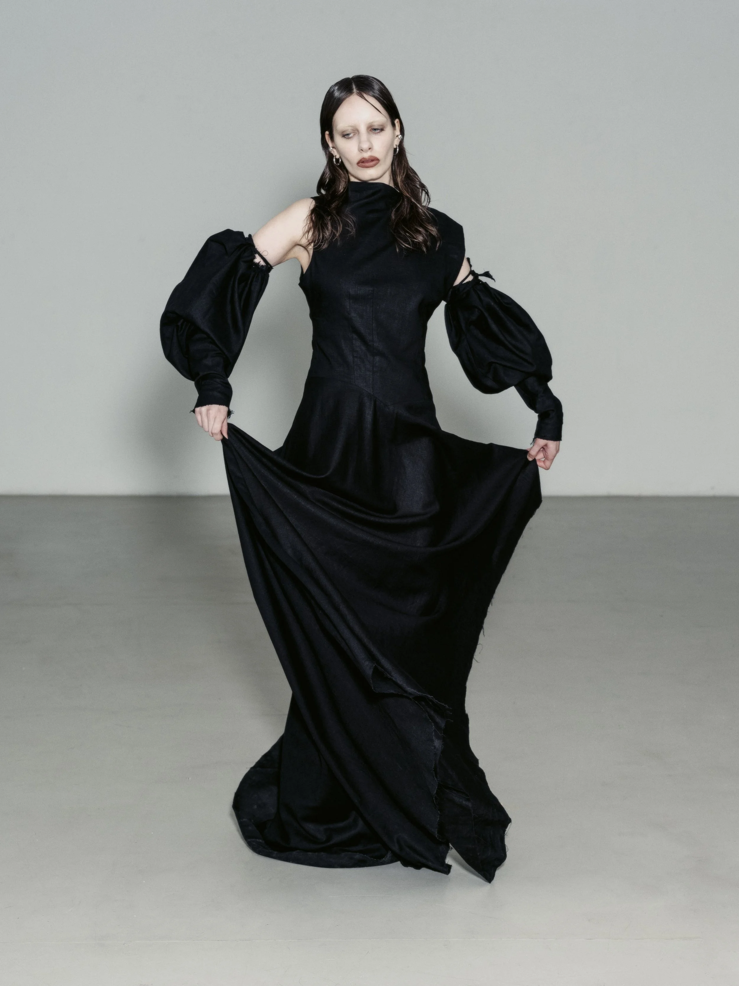 Frau in einem langen schwarzen Kleid mit Puffärmeln posiert vor einer neutralen Wand.