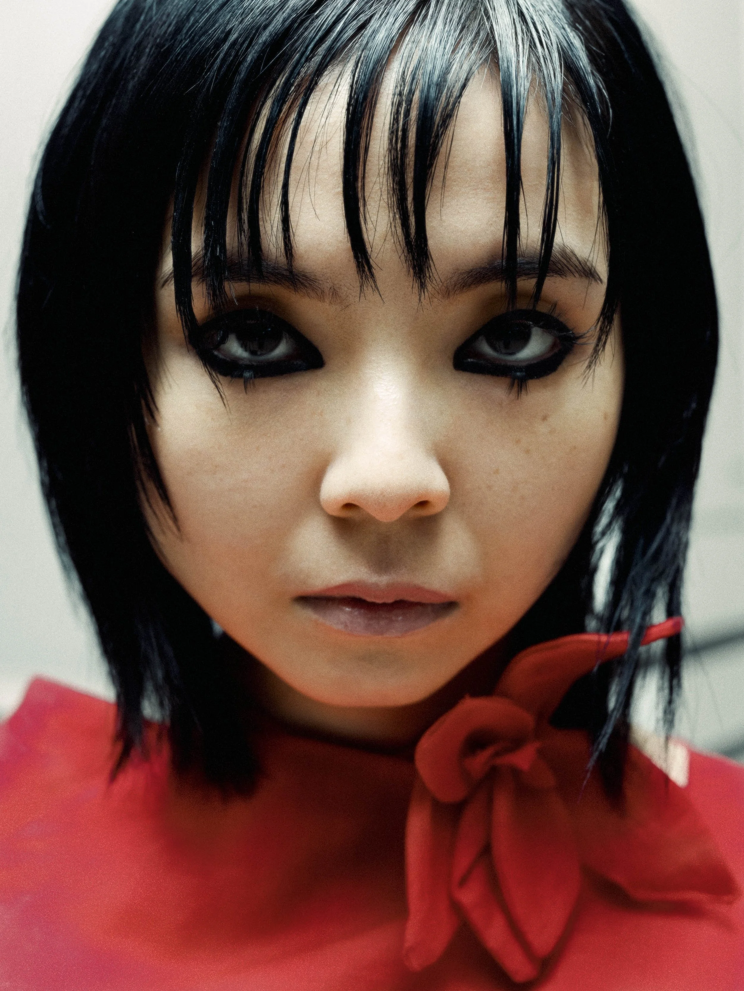 Nahaufnahme eines künstlichen Gesichts mit schwarzen Haaren, dunklem Make-up um die Augen und rotem Kleid mit Schleifenakzent.