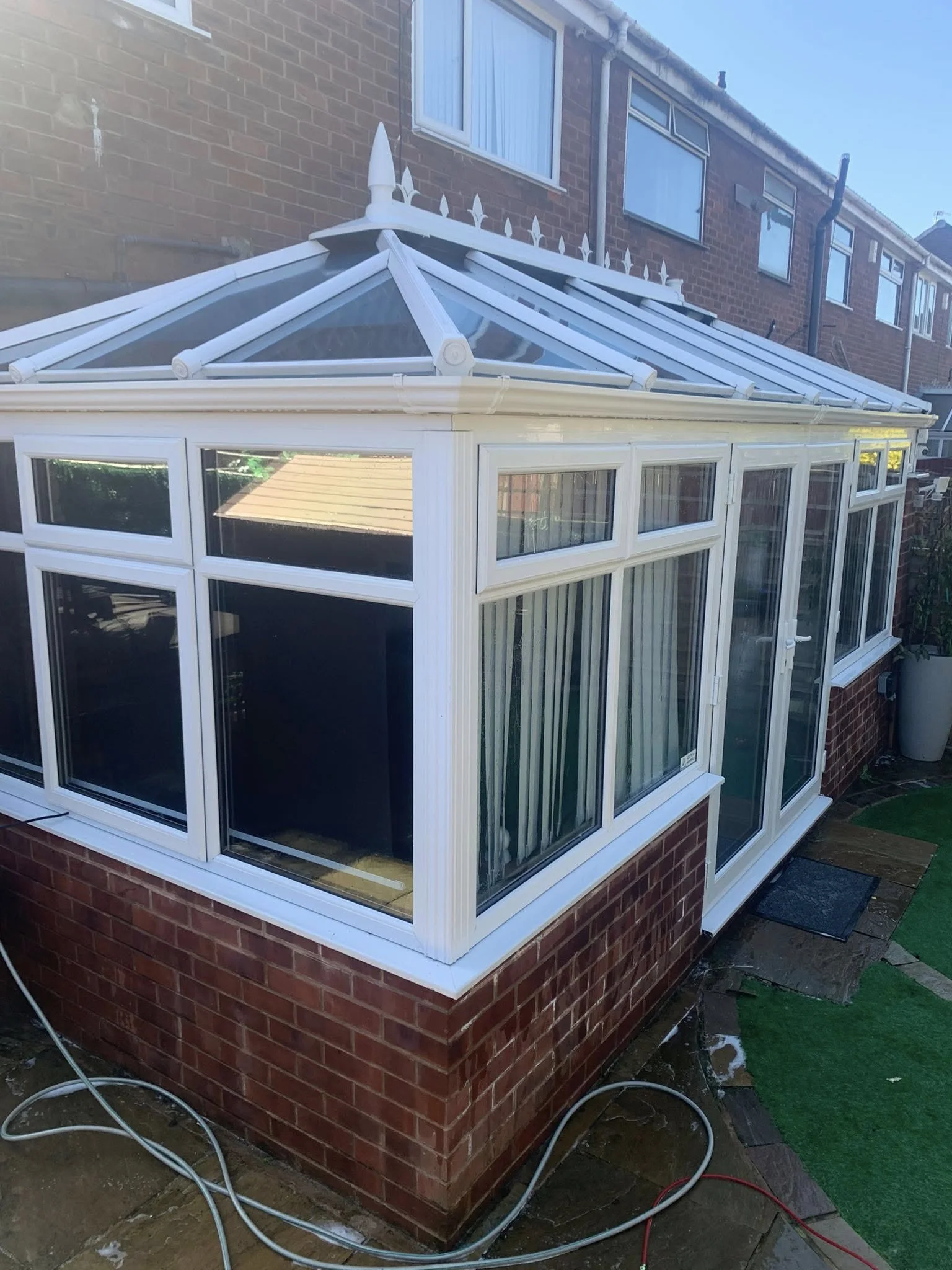 Sliding glass door with dark green frame installed in a brick wall, leading to a patio area with plants and outdoor furniture.