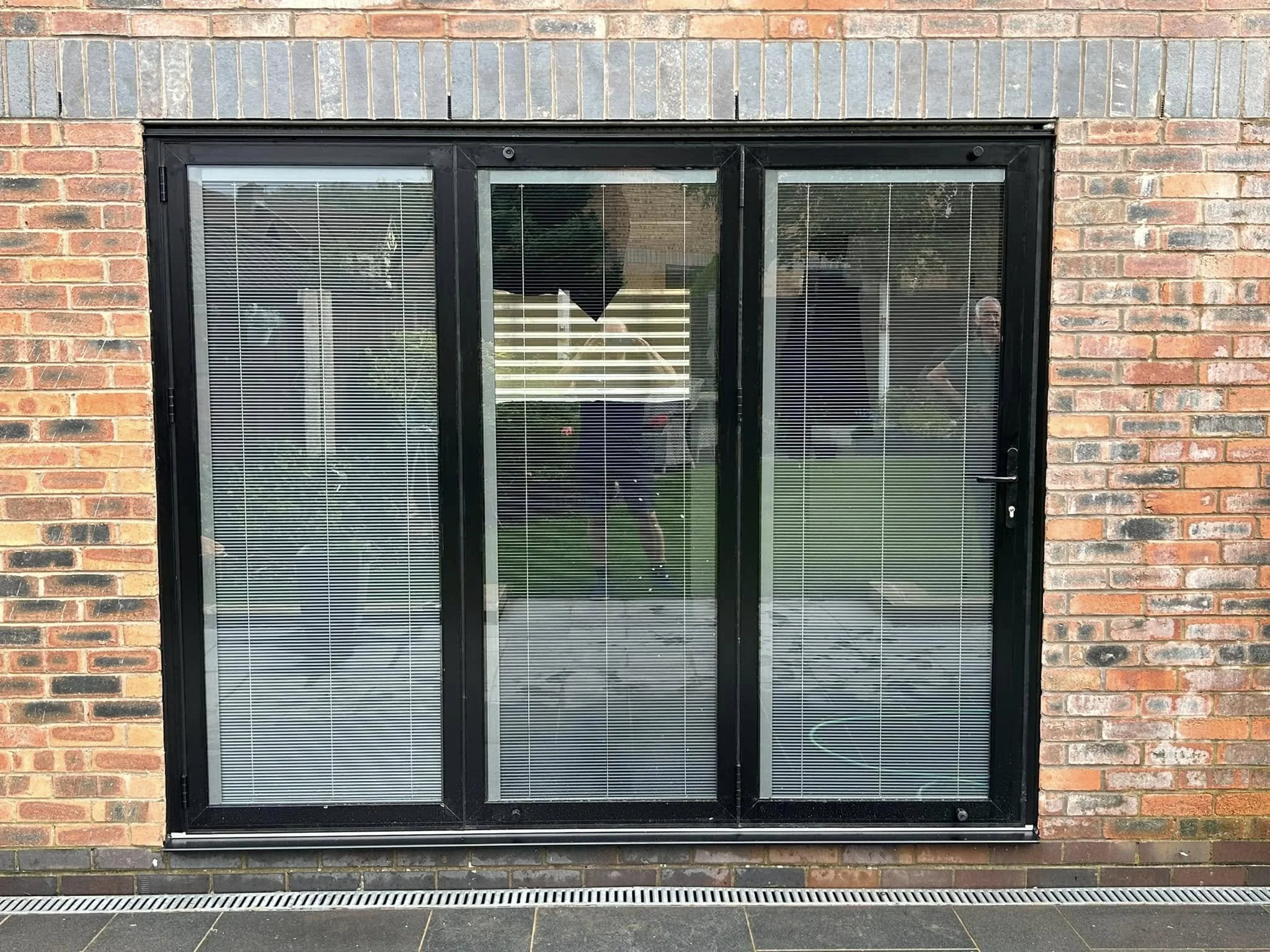 A sliding glass door with black frame and blinds, set into a red brick wall exterior.