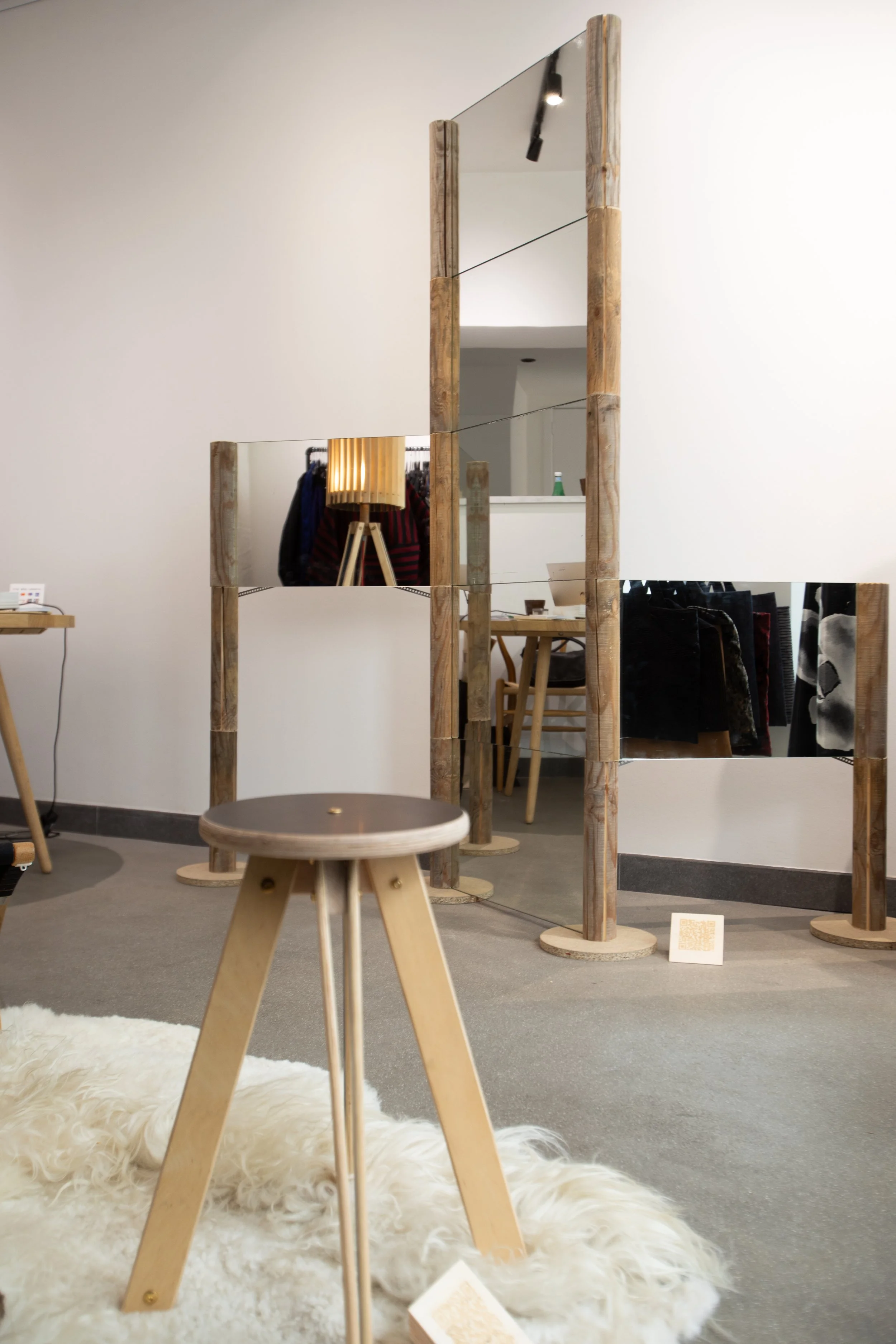 A standing wooden room divider with mirror panels in a modern room. Various furnishings, including a small round table and a fluffy white rug, are visible.