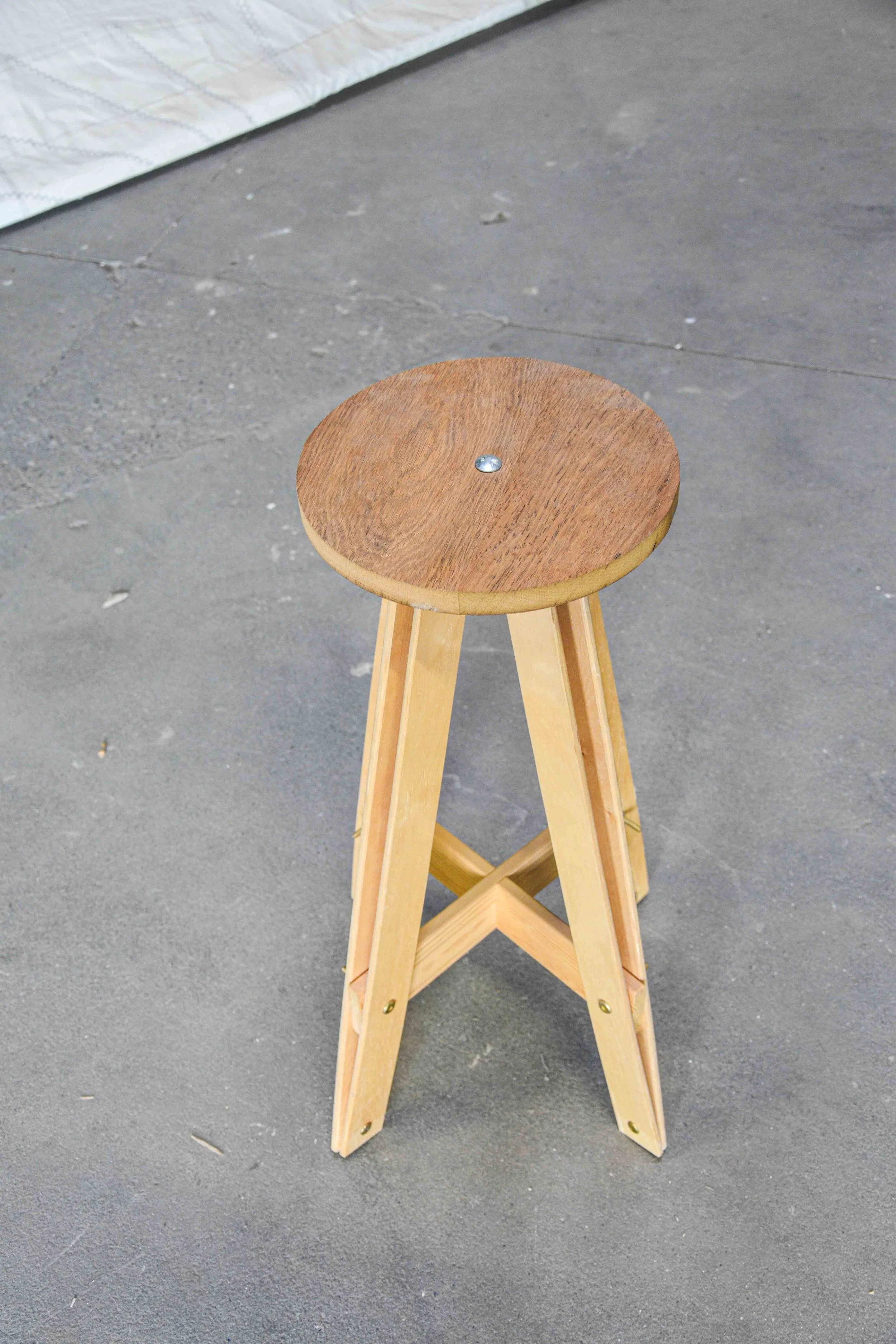 A wooden stool with four legs on a concrete floor.