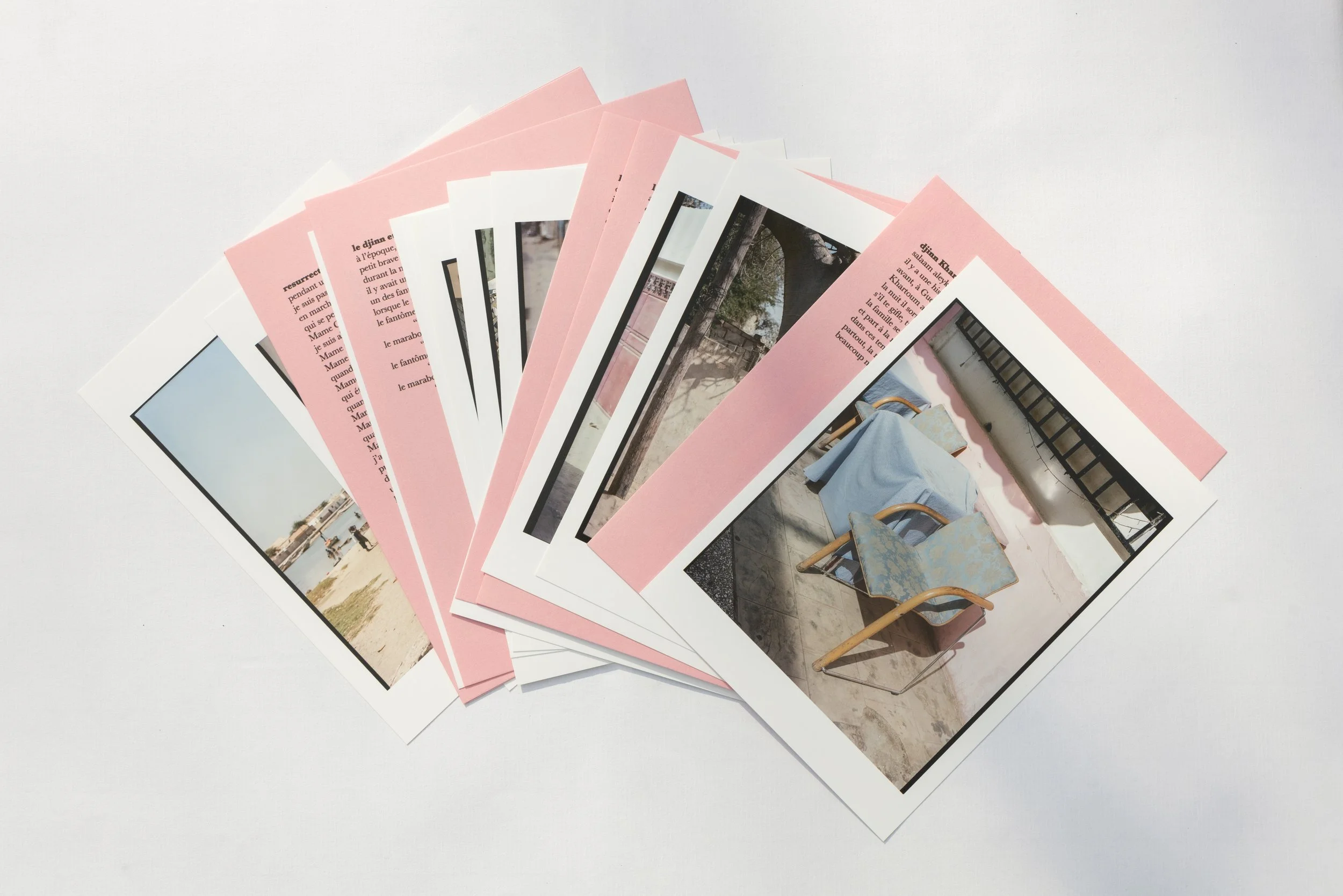 A set of printed photographs and pink-bordered papers arranged in a fan shape on a white surface, with images of outdoor scenes and a close-up of chairs with light blue covers.