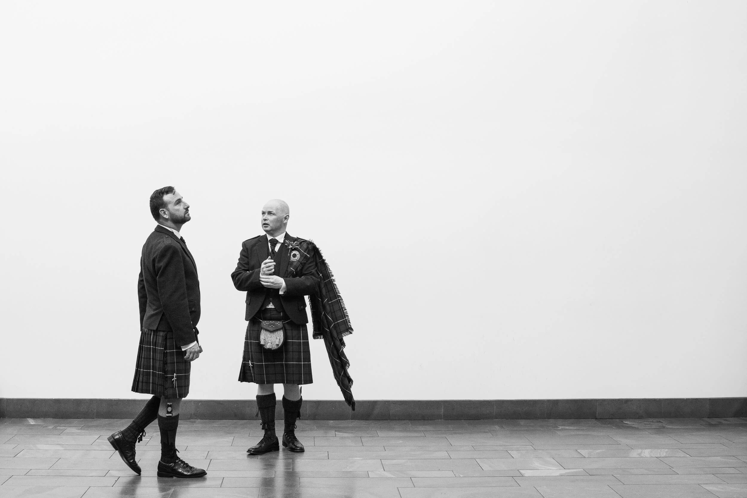 Two men in kilts — the scale and stillness of a quiet moment before a Scottish wedding, captured by Robert Ozog