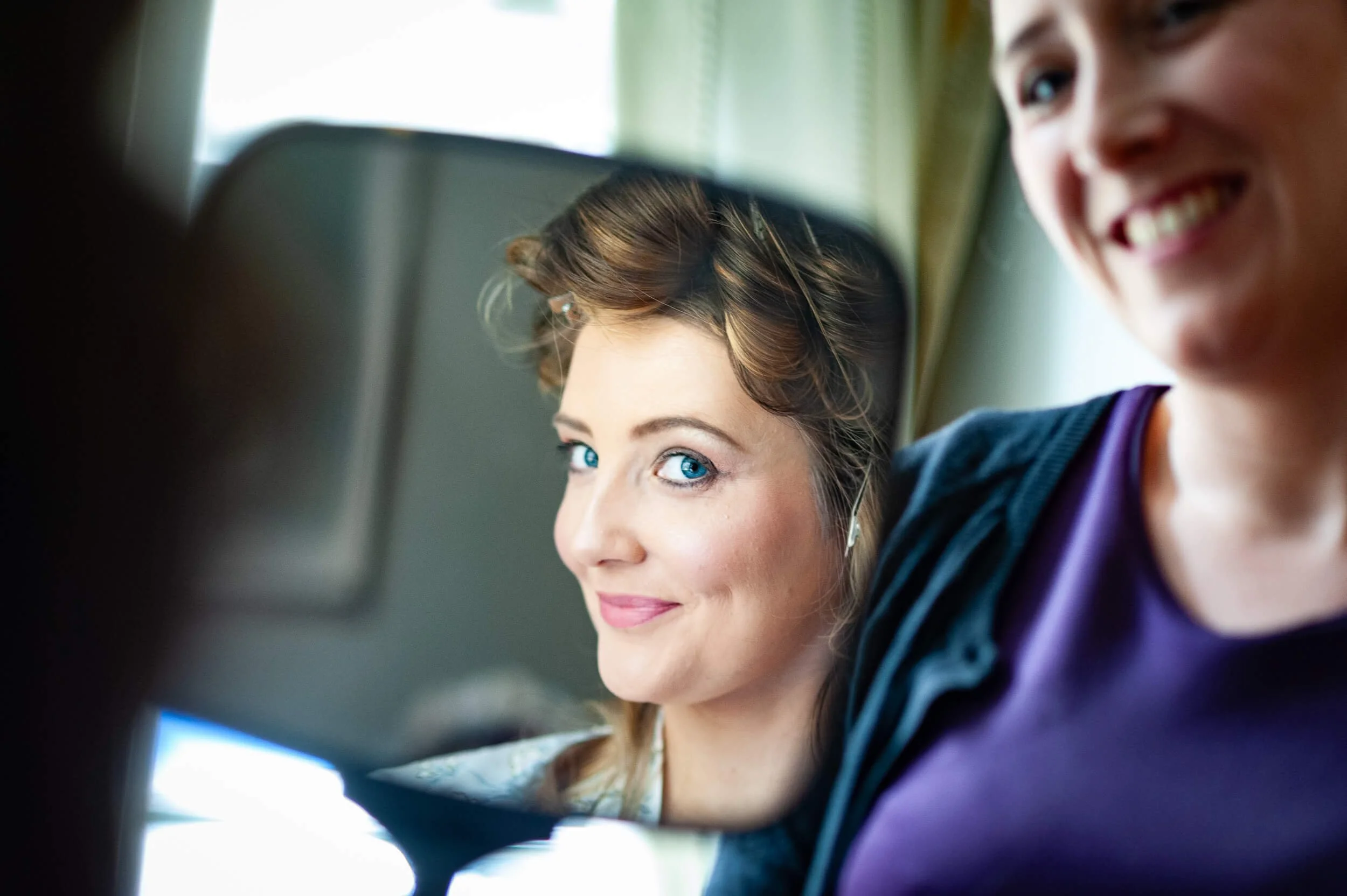 A woman with bright blue eyes and brown hair, smiling and taking a selfie with a man with a bright smile, both sitting on an airplane.