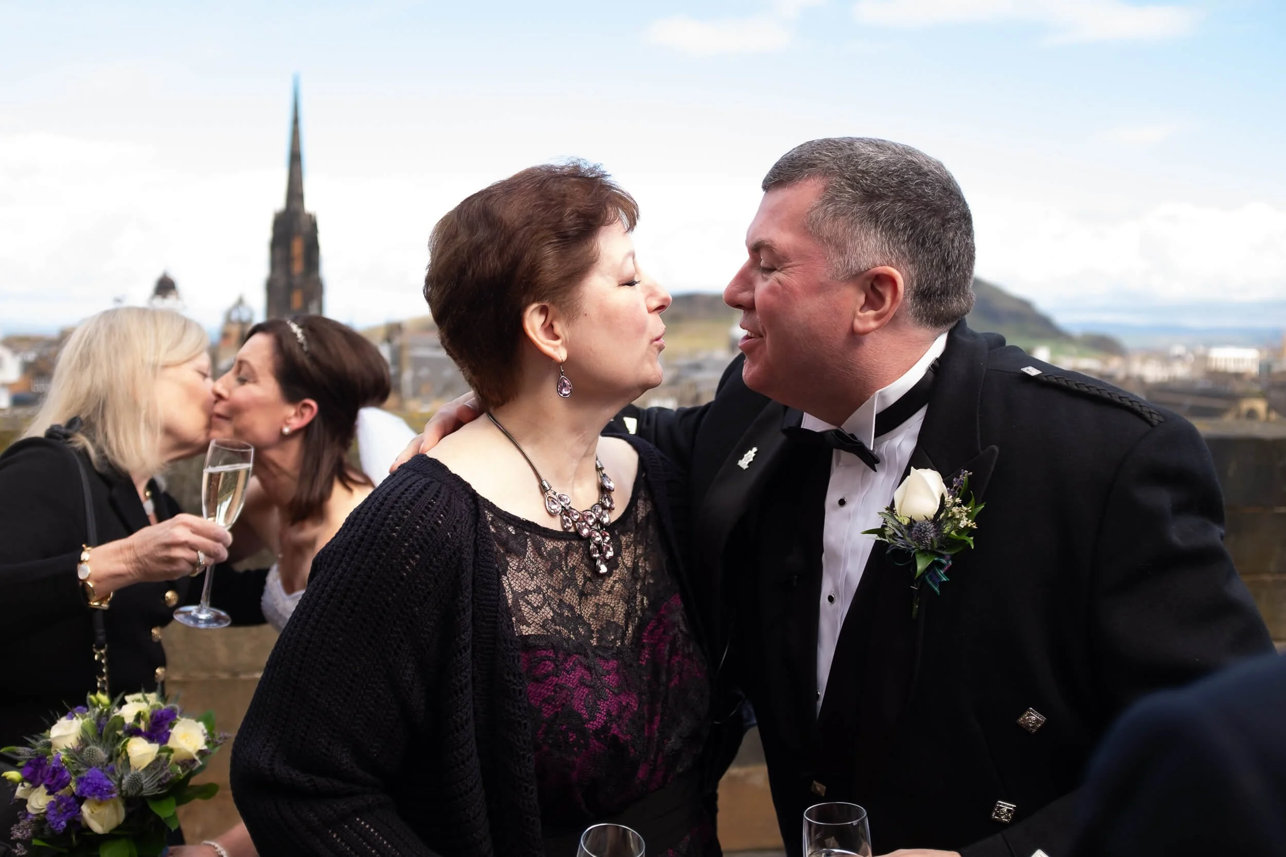 Wedding guests celebrating on the ramparts of Edinburgh Castle with Arthur's Seat in the background — documentary wedding photography Scotland