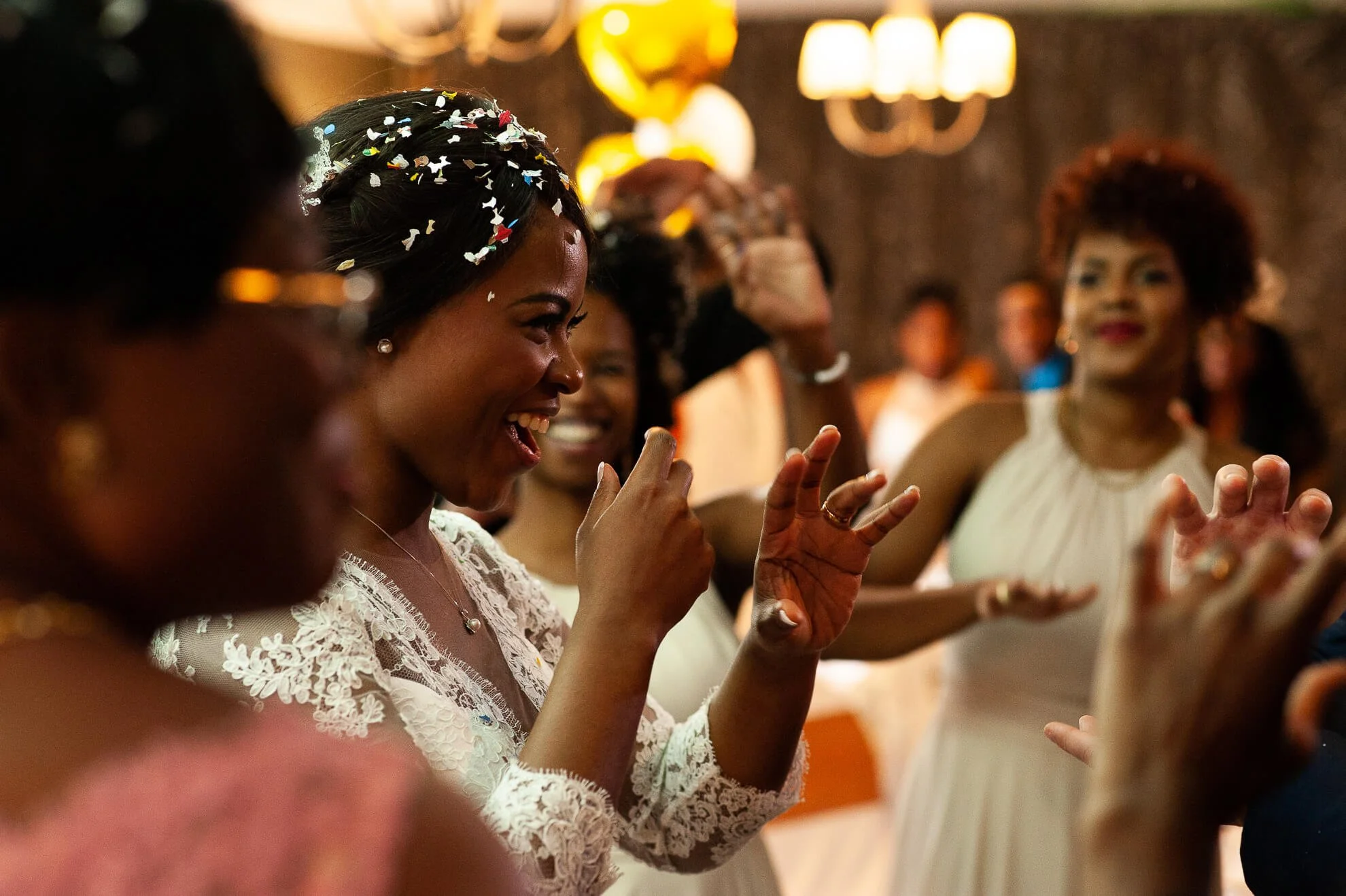 Women celebrating at a joyful indoor event, with one woman in the center throwing confetti and laughing.