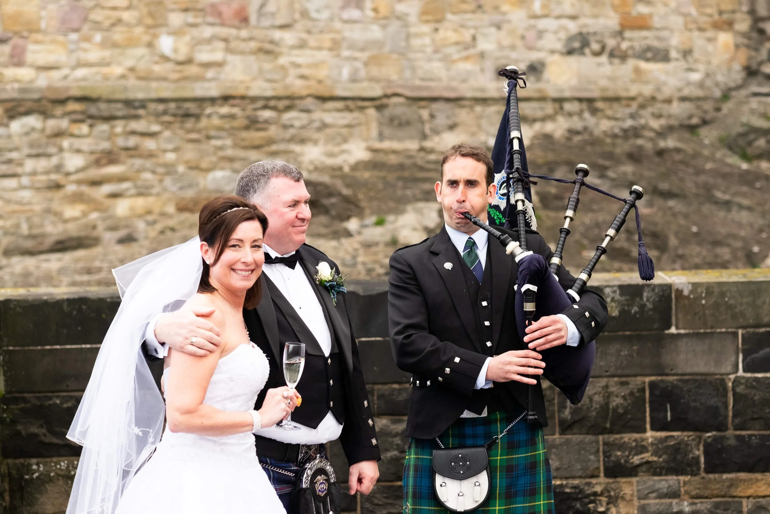 Bride and groom with Scottish bagpiper on the ramparts of Edinburgh Castle — wedding photography Scotland