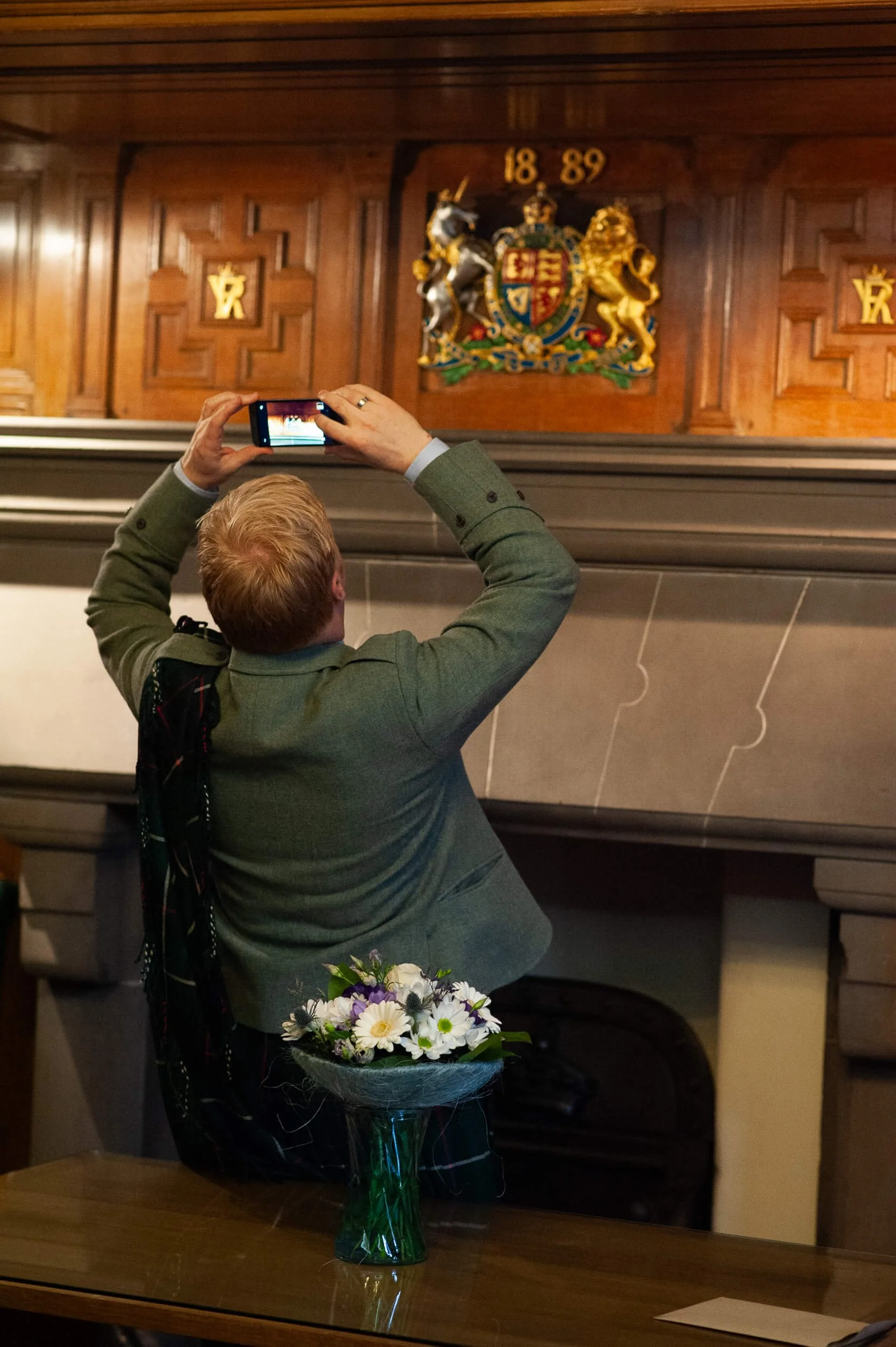 Wedding guest photographing the royal coat of arms inside Edinburgh Castle — Scottish wedding documentary photography