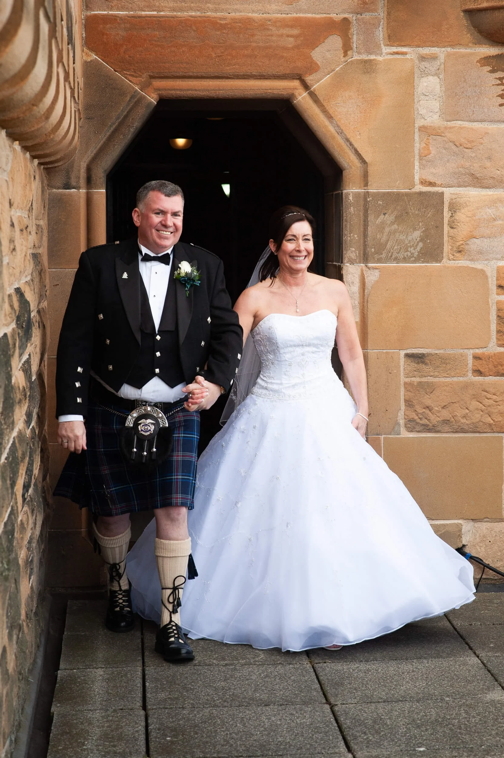 Bride and groom walking through stone archway at Edinburgh Castle — wedding photography Scotland
